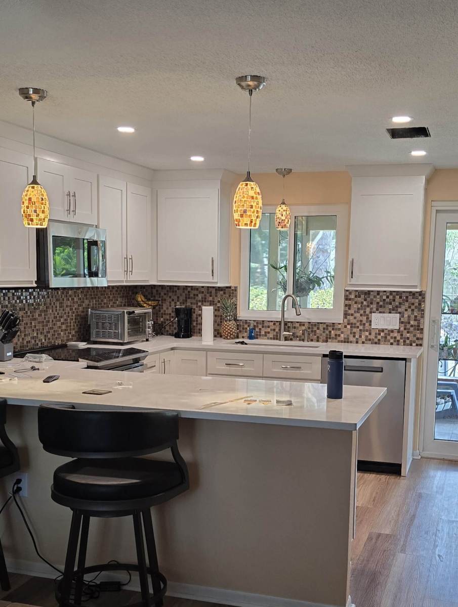 Remodeled kitchen with white cabinets, quartz peninsula and glass pendant lights