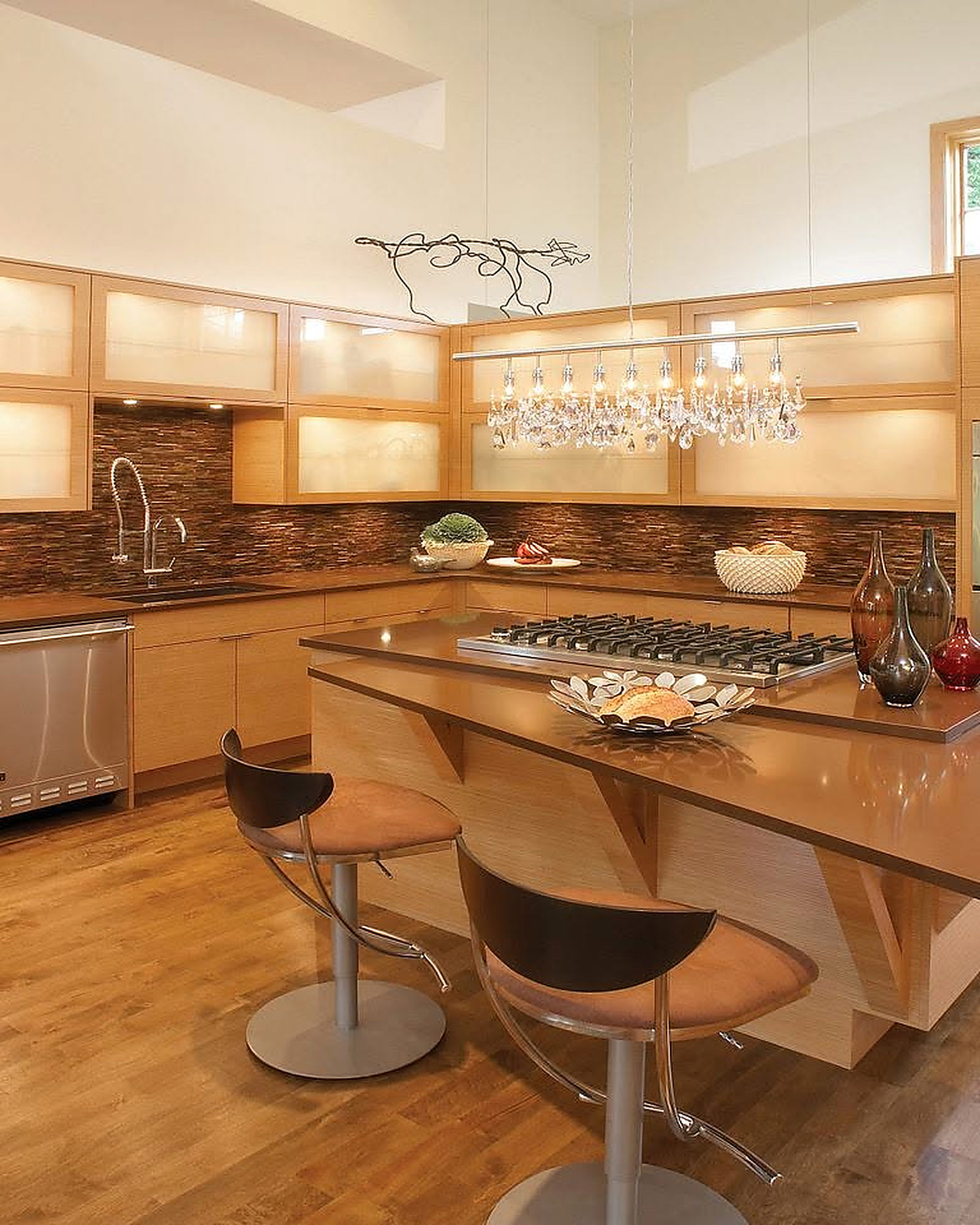 Contemporary kitchen with light wood cabinets, a crystal chandelier and bar seating