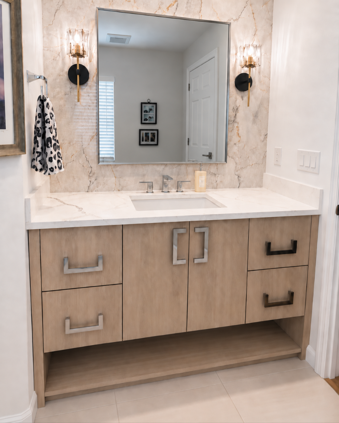 Powder room vanity with a marble backsplash, framed mirror and wall sconces