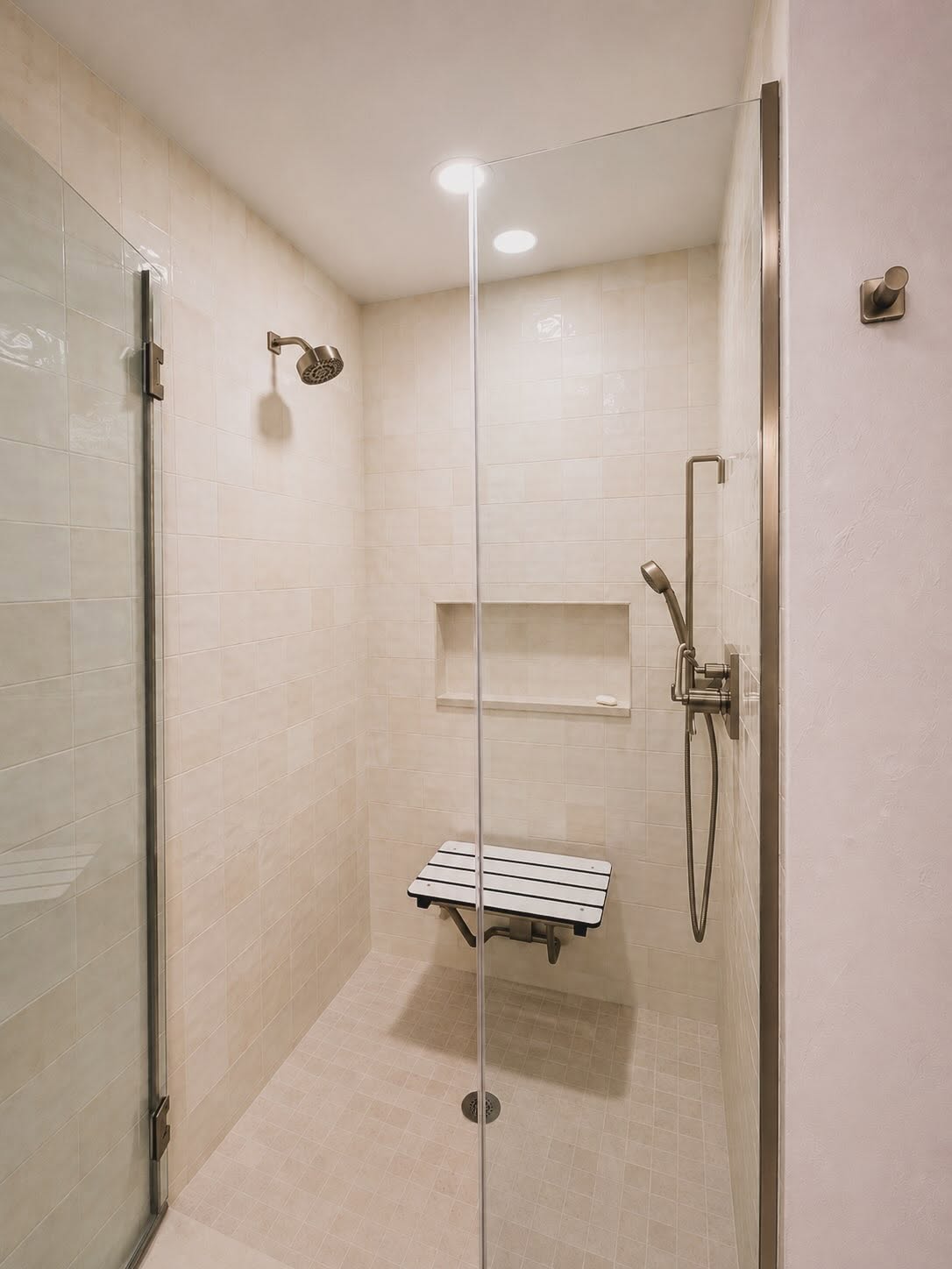 Walk-in shower with cream tile, a fold-down bench seat and handheld sprayer