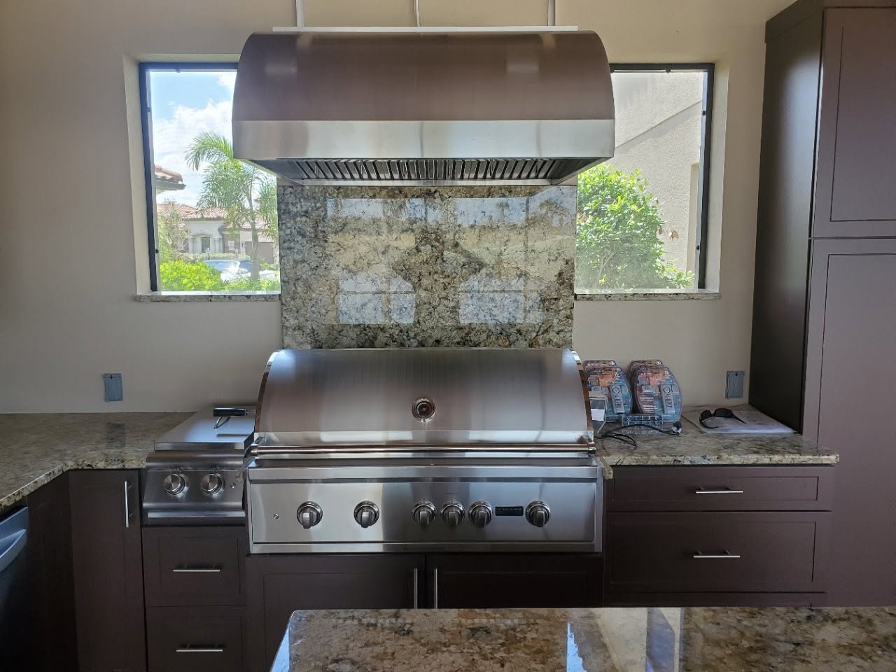 Outdoor kitchen with a built-in stainless grill, granite counters and vent hood