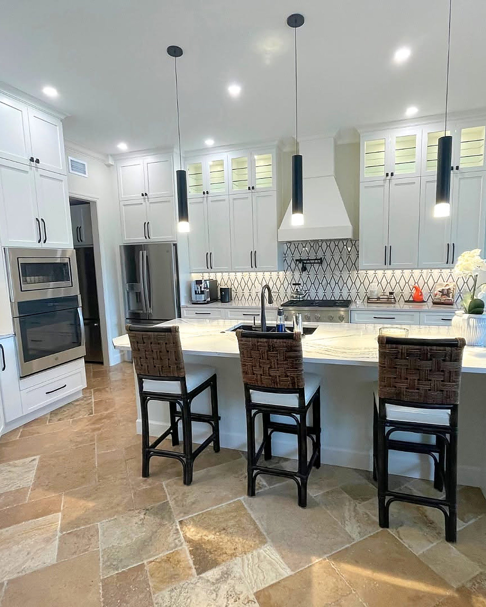 White kitchen with a large island, pendant lights and travertine tile floor