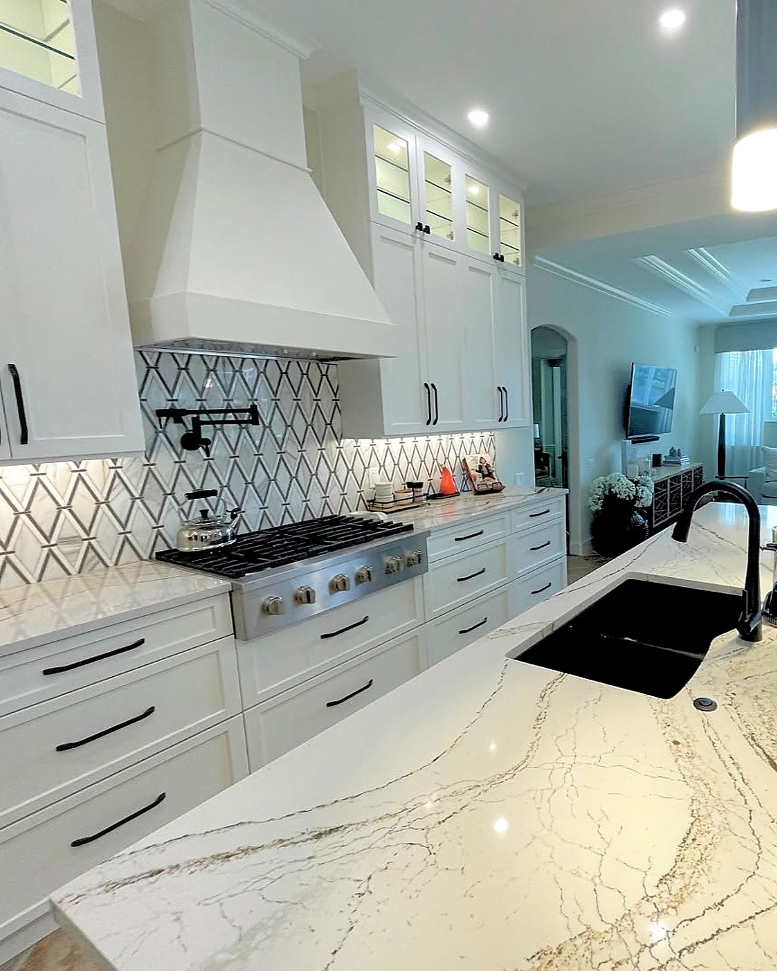 White kitchen with a plaster range hood, geometric backsplash and quartz counters