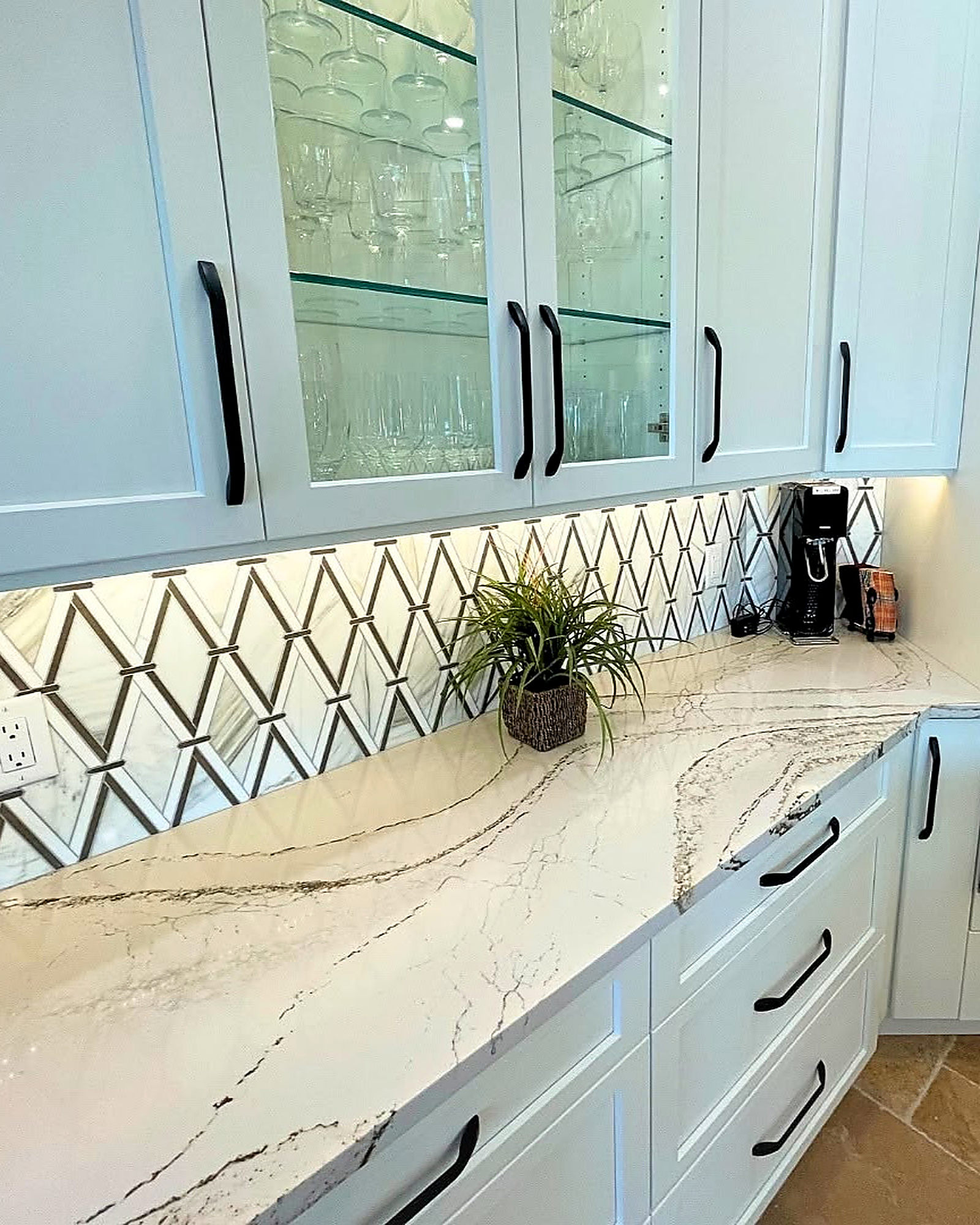 Glass-front upper cabinets above a mirrored geometric backsplash and quartz counter