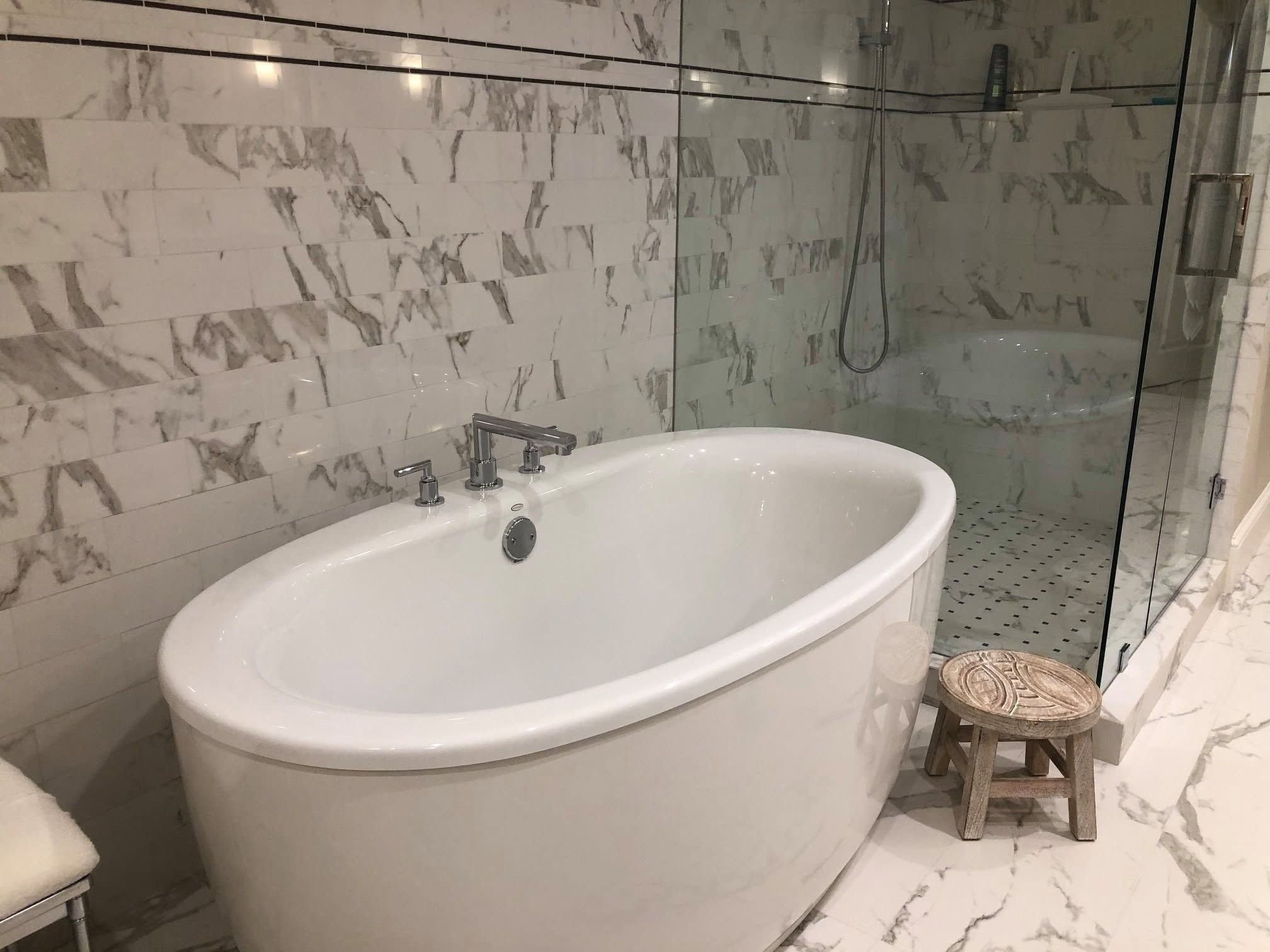 Freestanding soaking tub beside a glass shower with marble-look tile