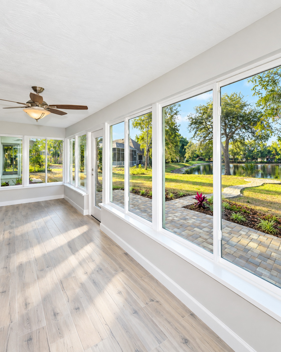 Enclosed sunroom with floor-to-ceiling windows overlooking a pond