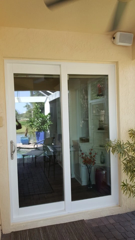 White sliding glass patio door leading to a brick paver pool deck