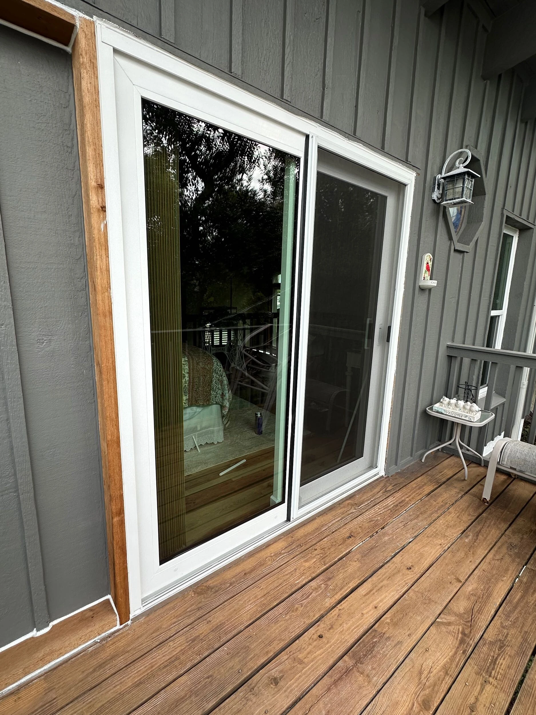 White sliding glass door installed in a gray board and batten wall above a wood deck