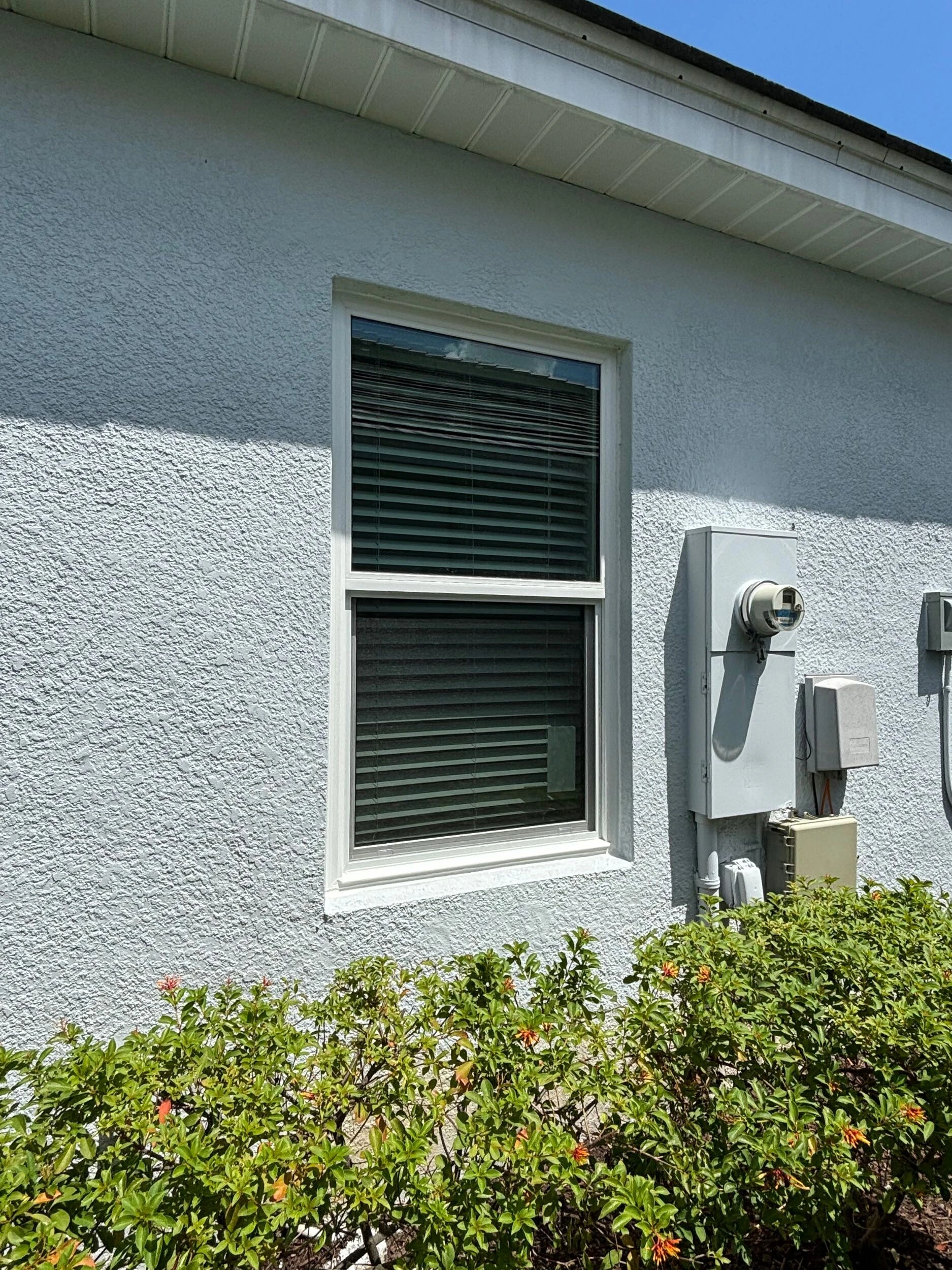 New single hung window on a light blue stucco wall beside the electrical meter