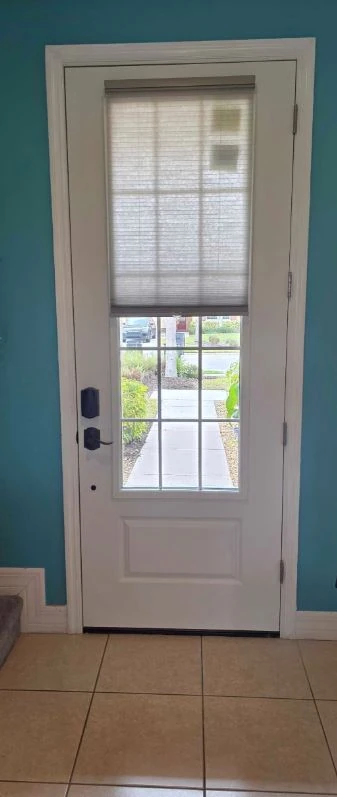 White entry door with a divided-light glass panel and pleated shade