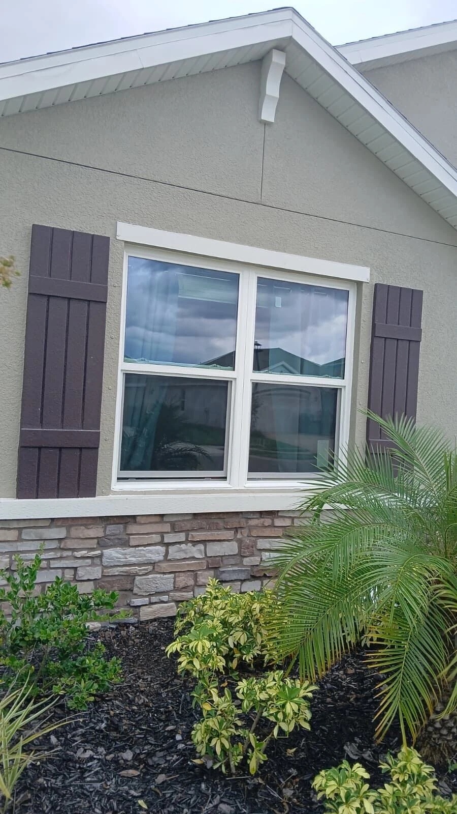 White replacement window with dark board and batten shutters and stone veneer