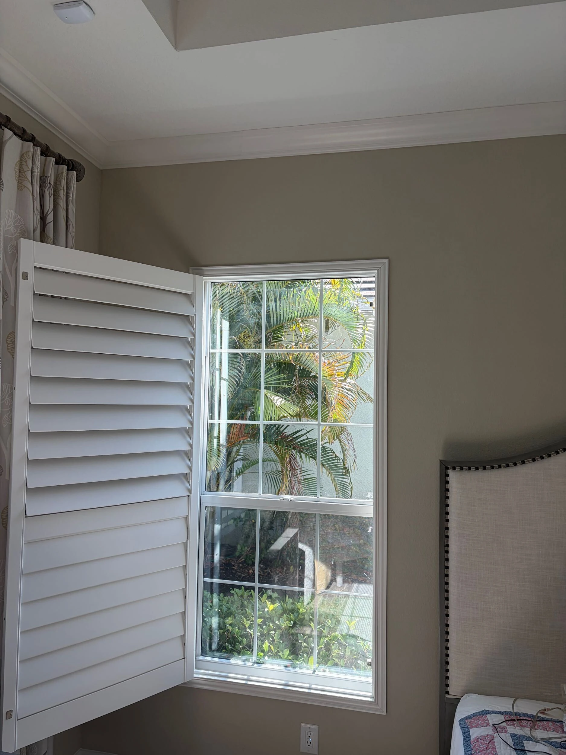 Bedroom window with white interior plantation shutters opened to the side