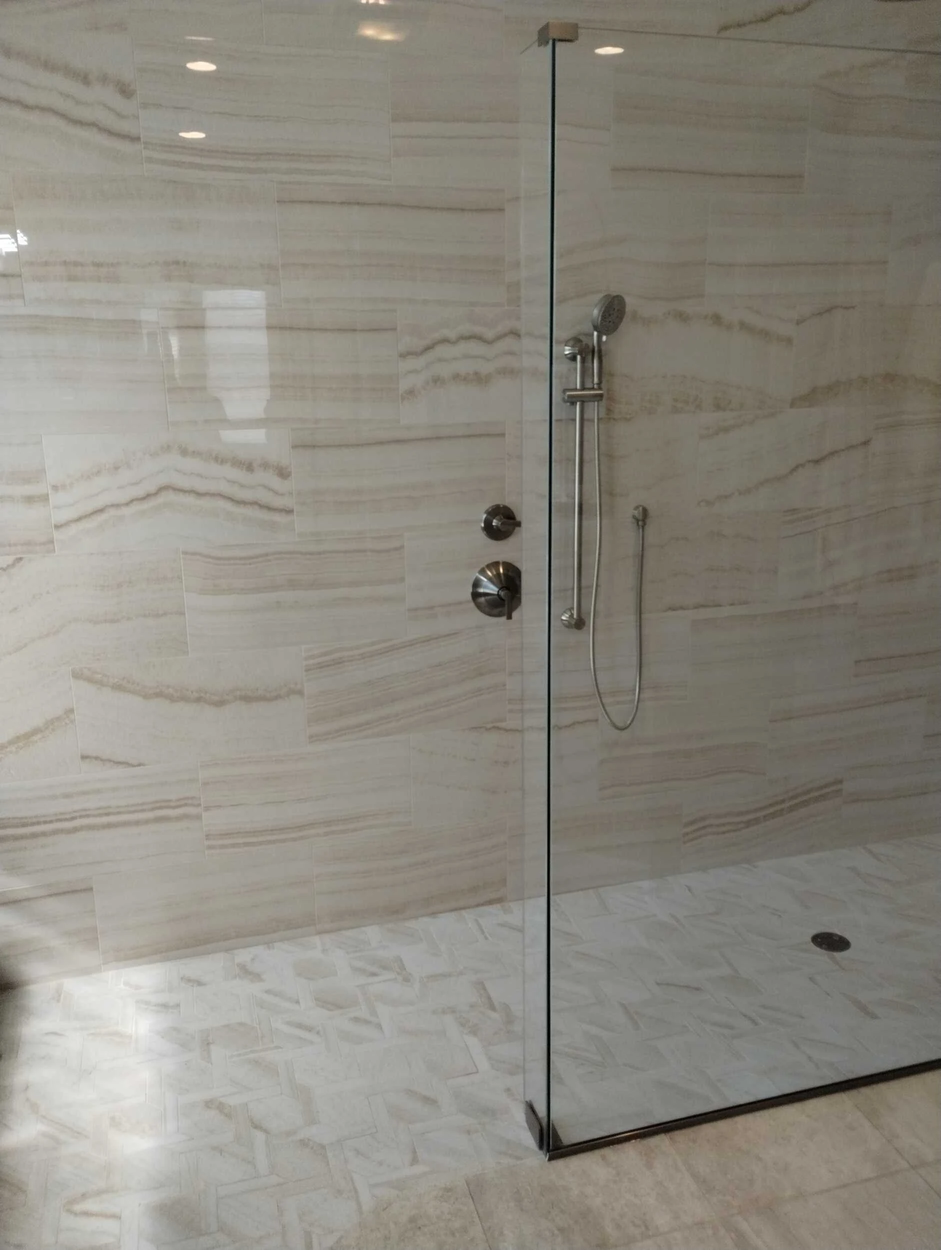 Frameless glass shower with cream stone-look tile and a herringbone tile floor