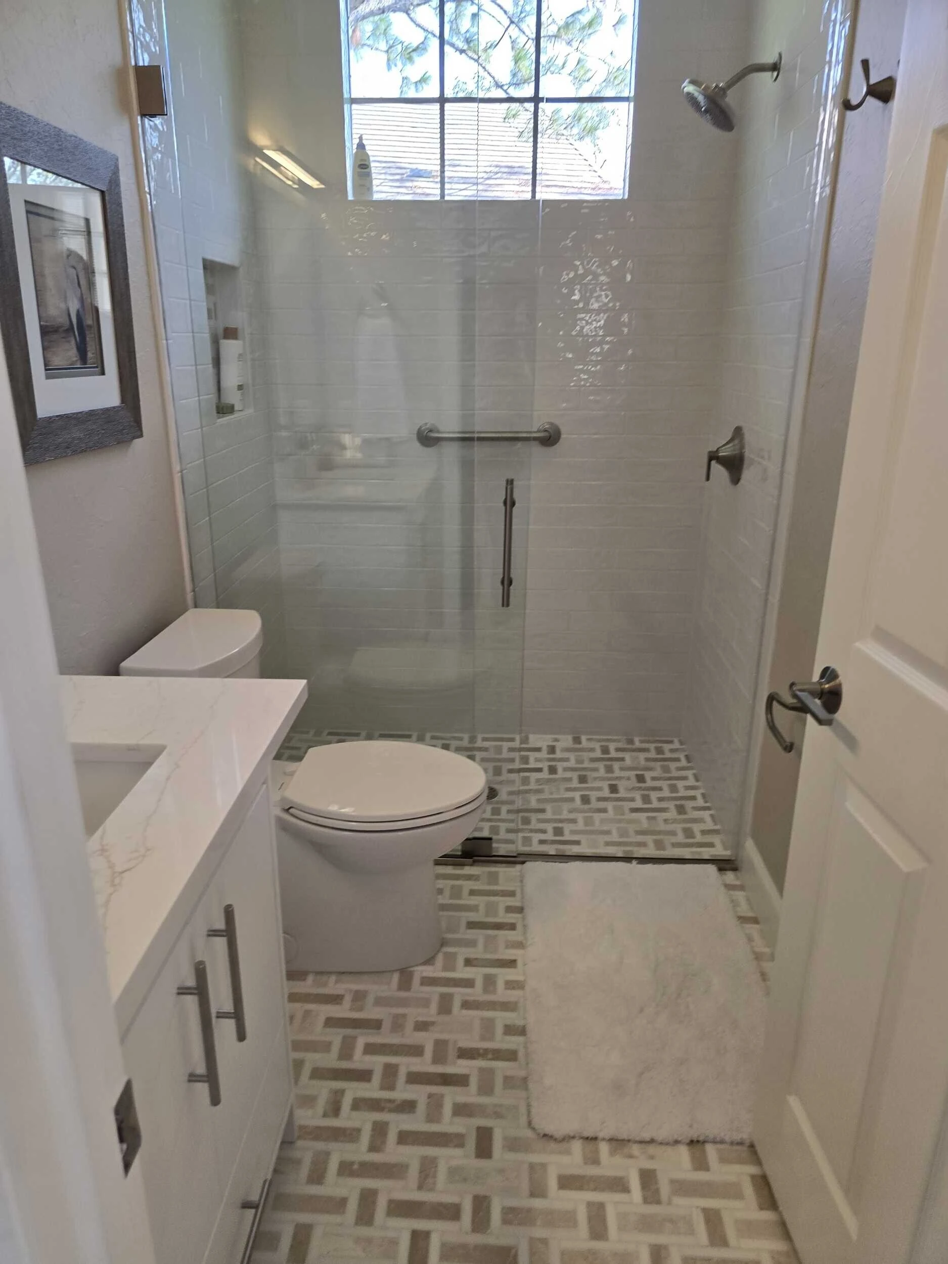 Remodeled bathroom with a glass walk-in shower, grab bar and patterned tile floor