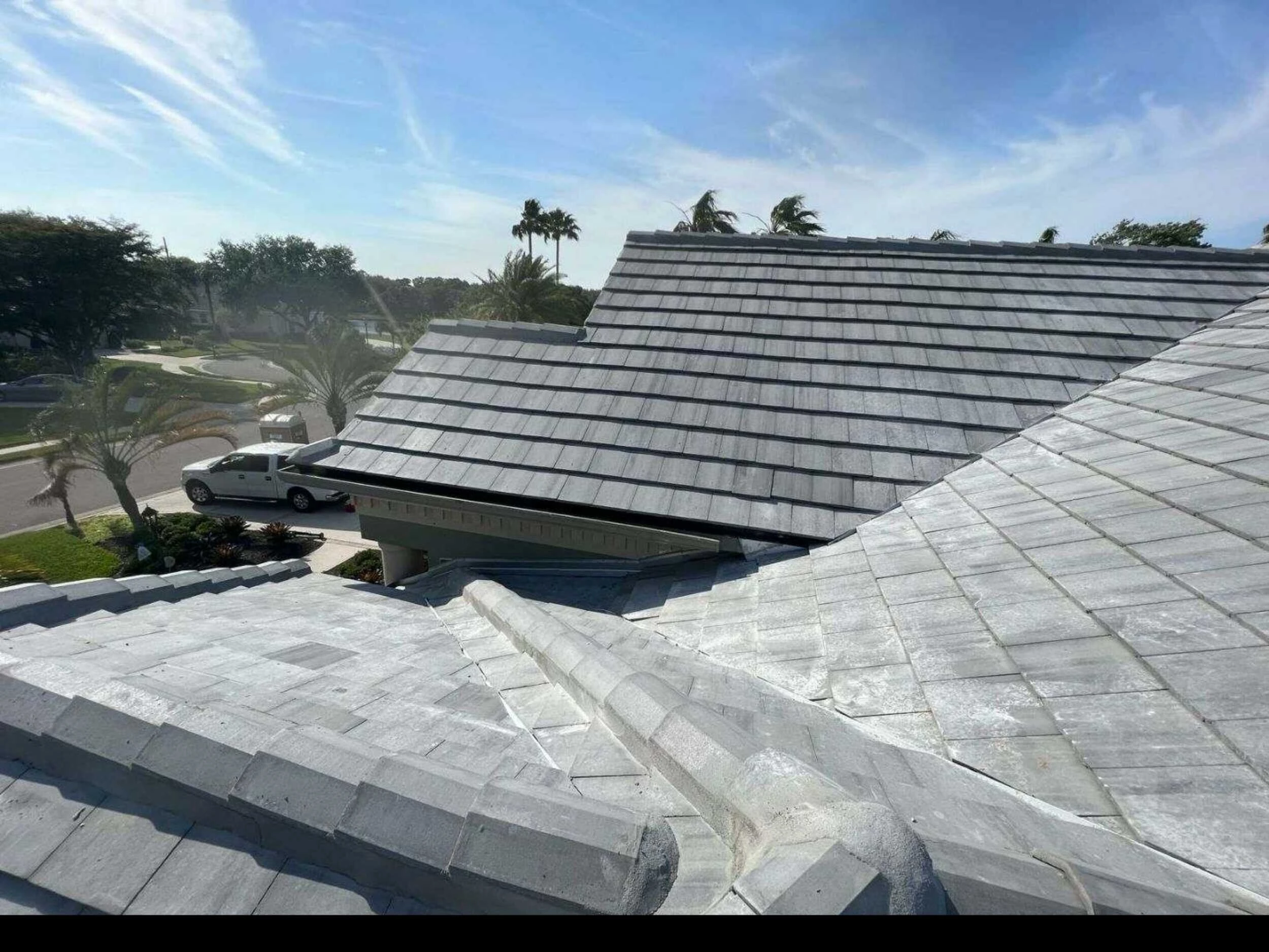 Gray tile roof replacement in progress on a home in a palm-lined neighborhood