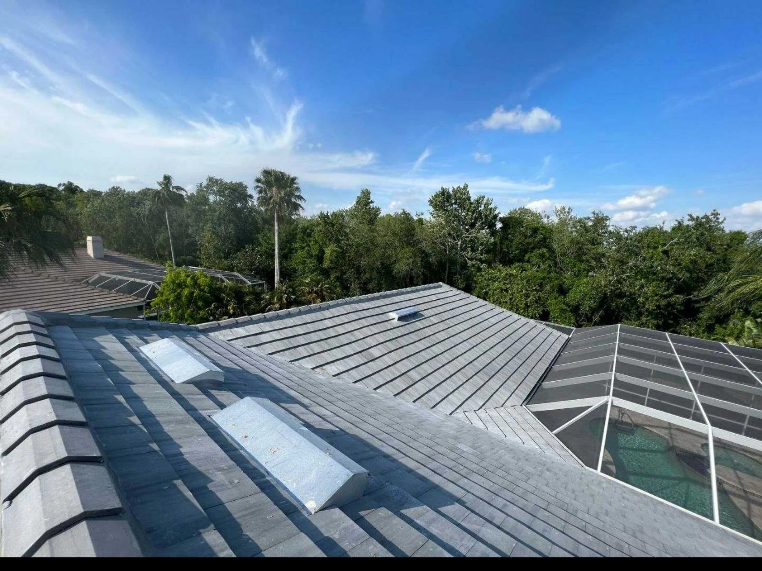 Gray concrete tile roof with skylights overlooking a screened pool cage
