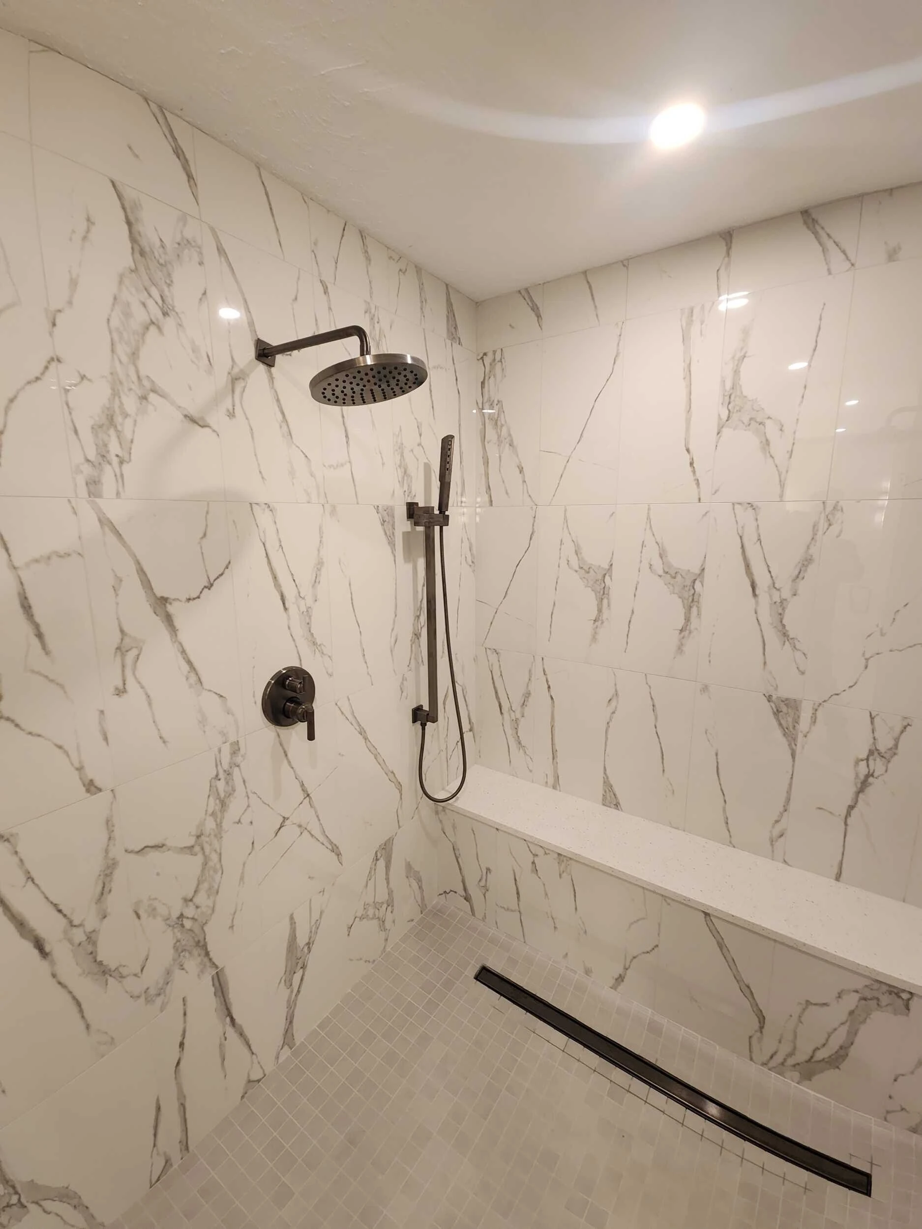Marble-look tiled shower with rain showerhead, handheld sprayer and a bench seat