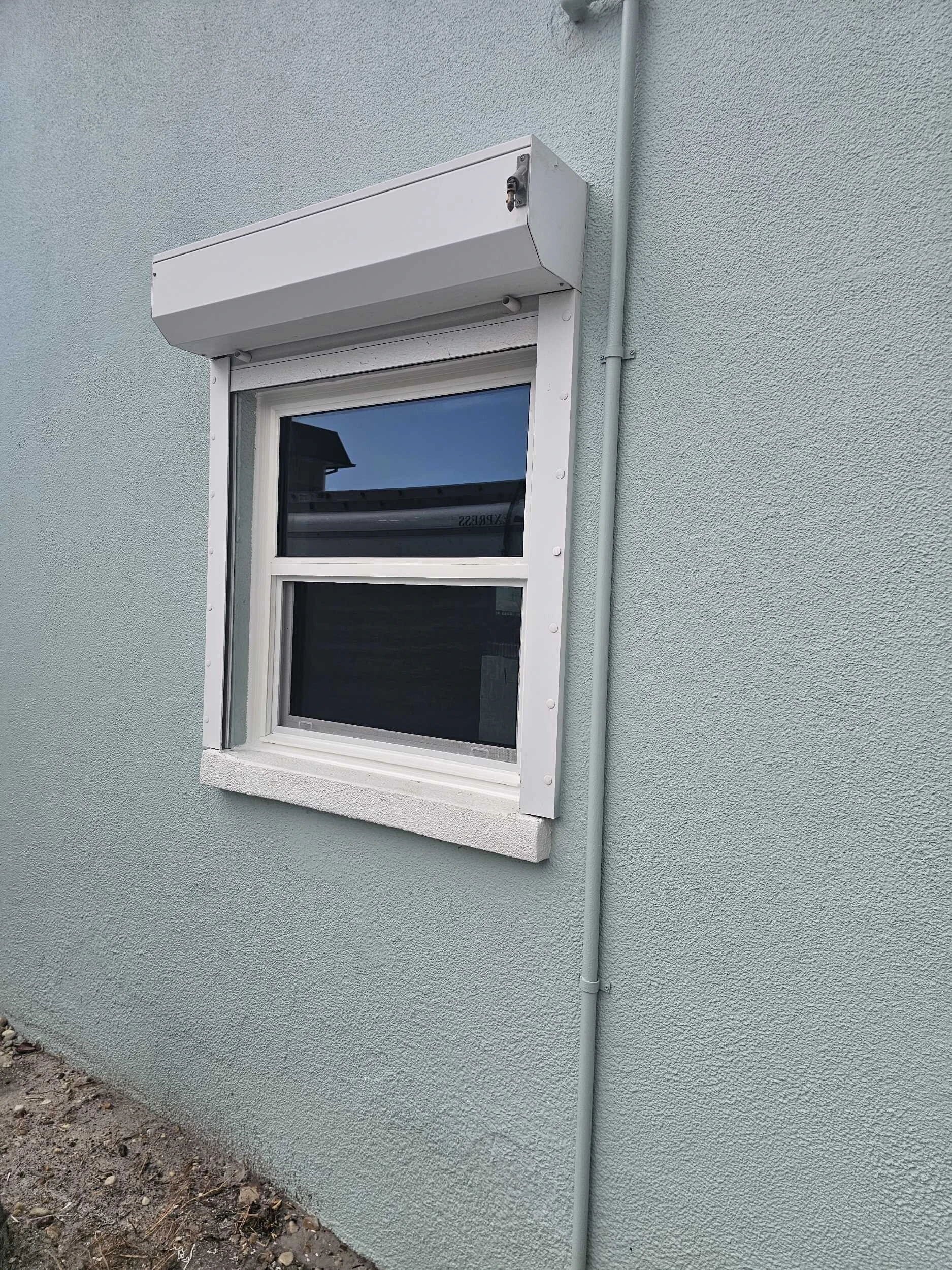 White impact window with a roll-down hurricane shutter on a light blue stucco wall