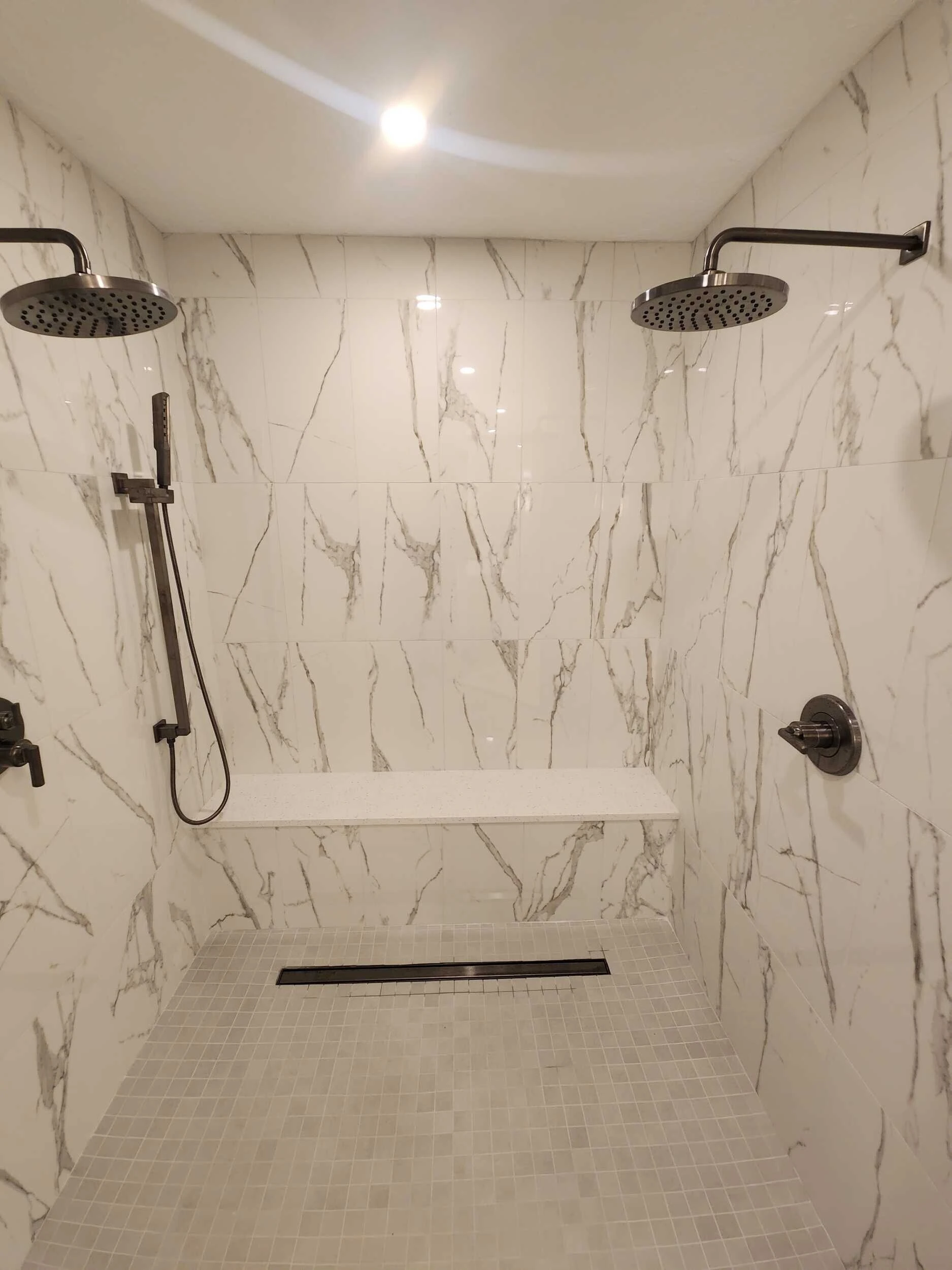 Walk-in shower with marble-look porcelain tile, dual rain showerheads and a built-in bench