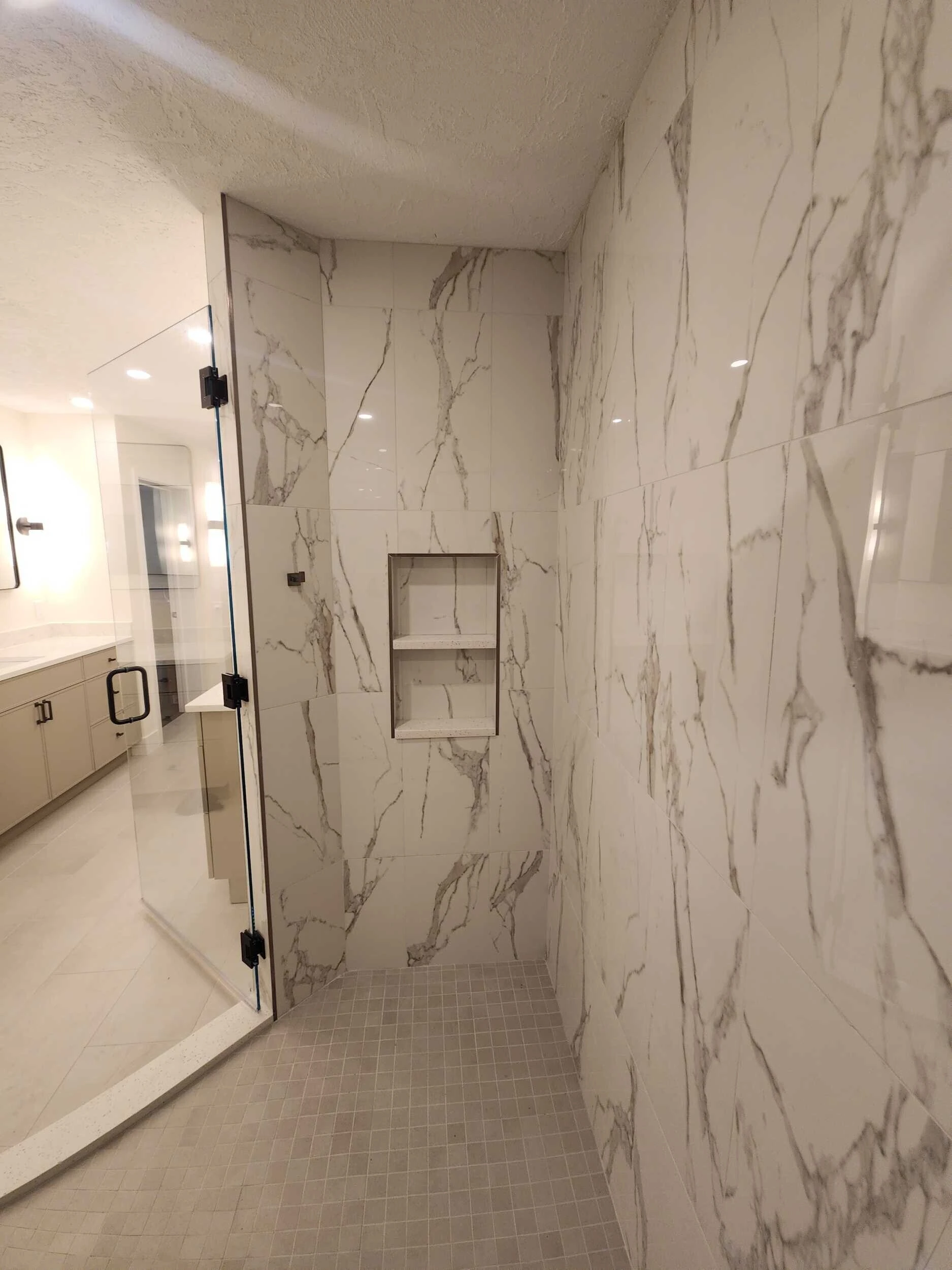 Glass-enclosed walk-in shower with marble-look tile walls and a recessed shelf niche