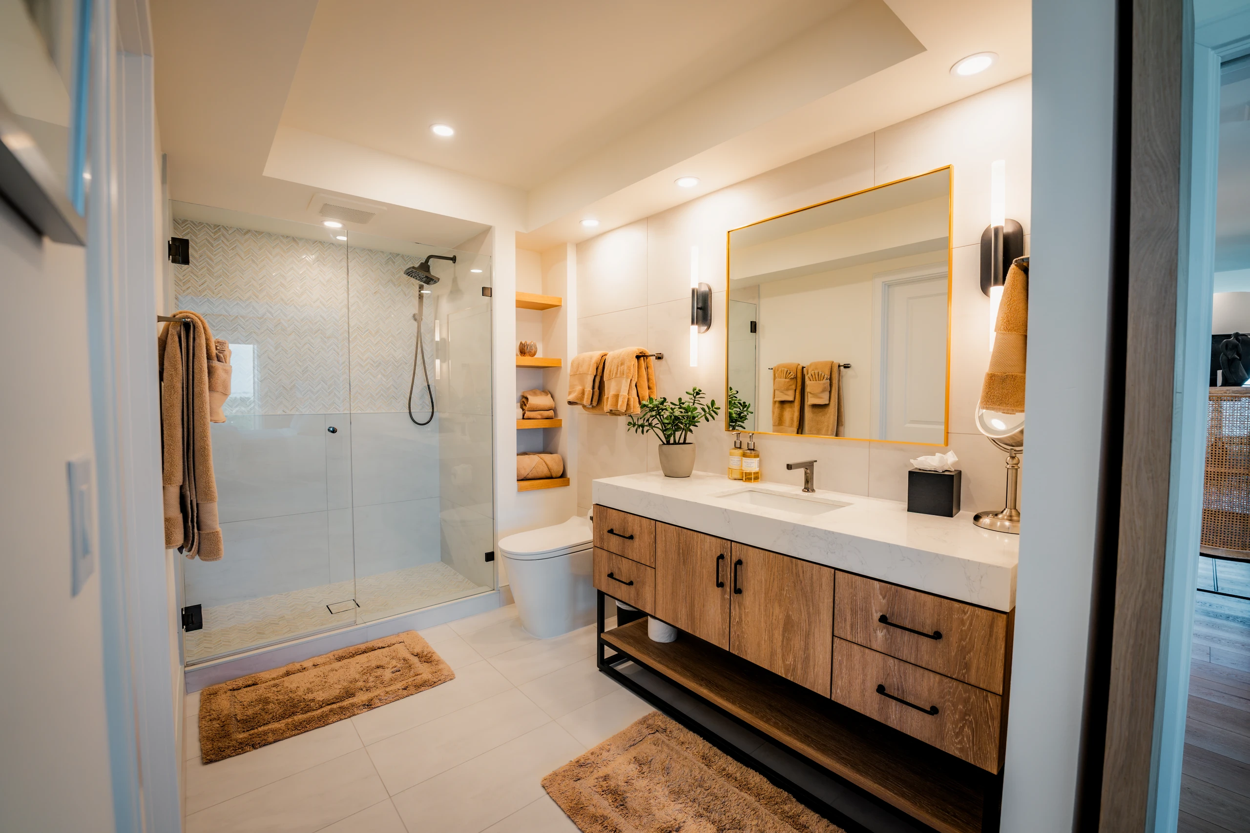 Remodeled bathroom with a glass shower, wood floating vanity and gold mirror