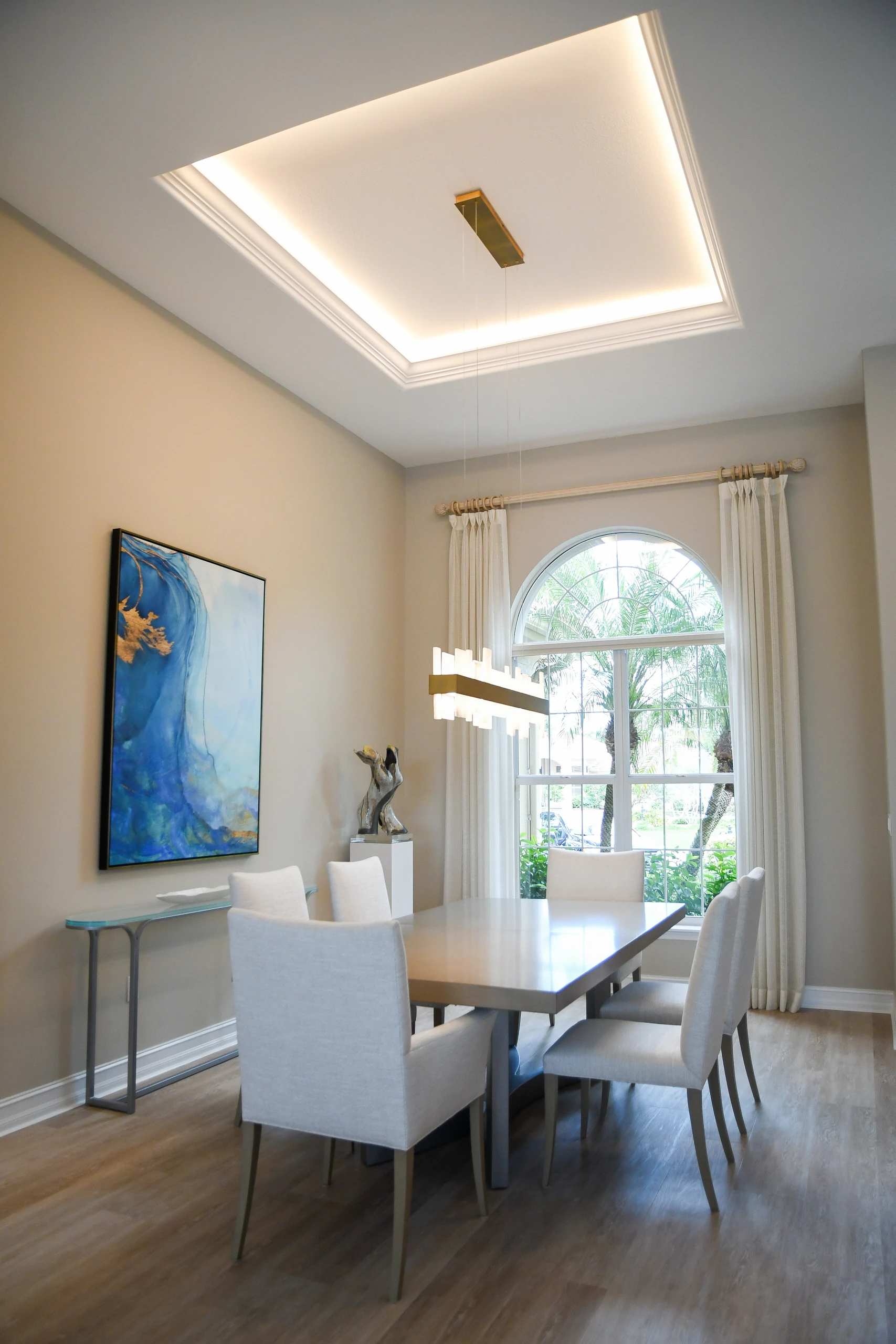 Dining room with a tray ceiling, linear pendant and arched window