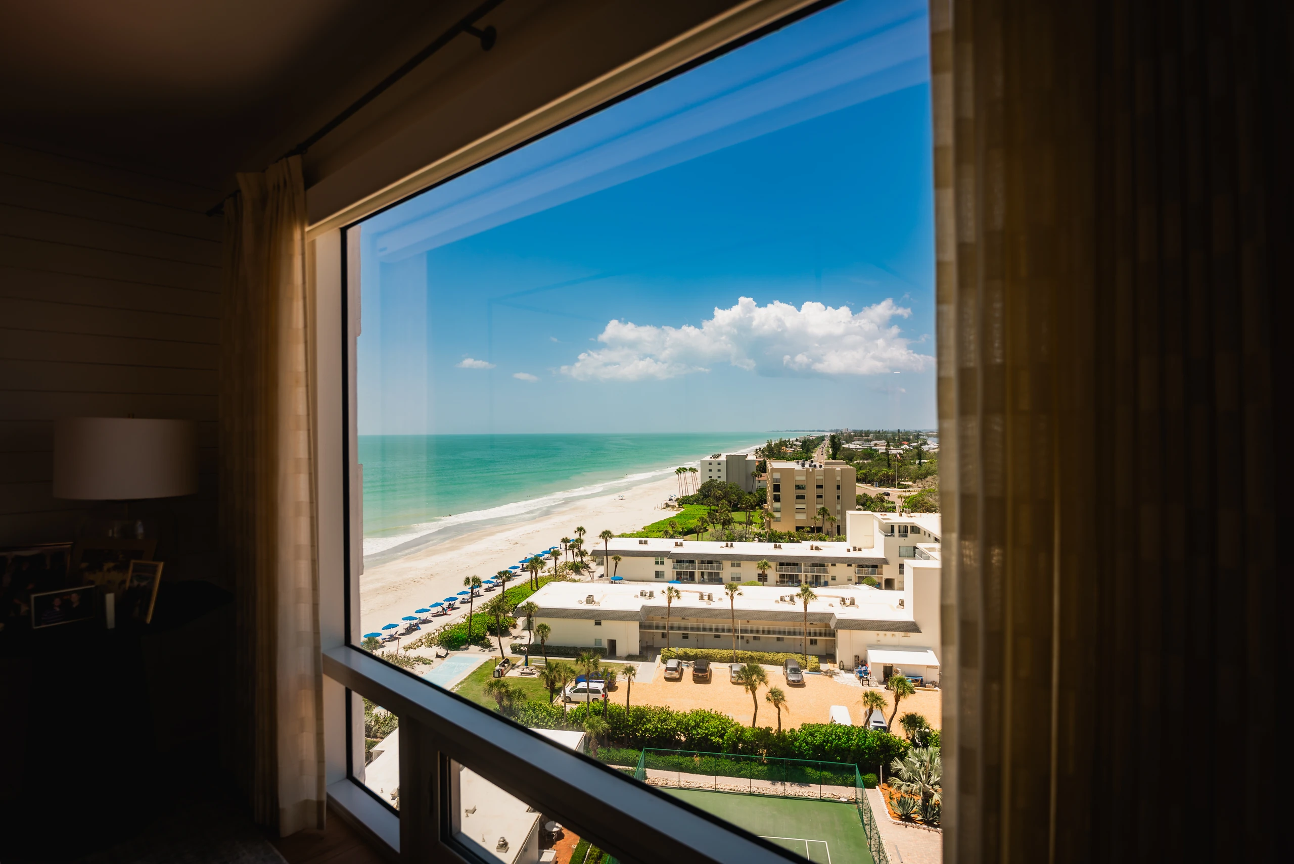 Picture window framing the beach and Gulf from a curtained condo room