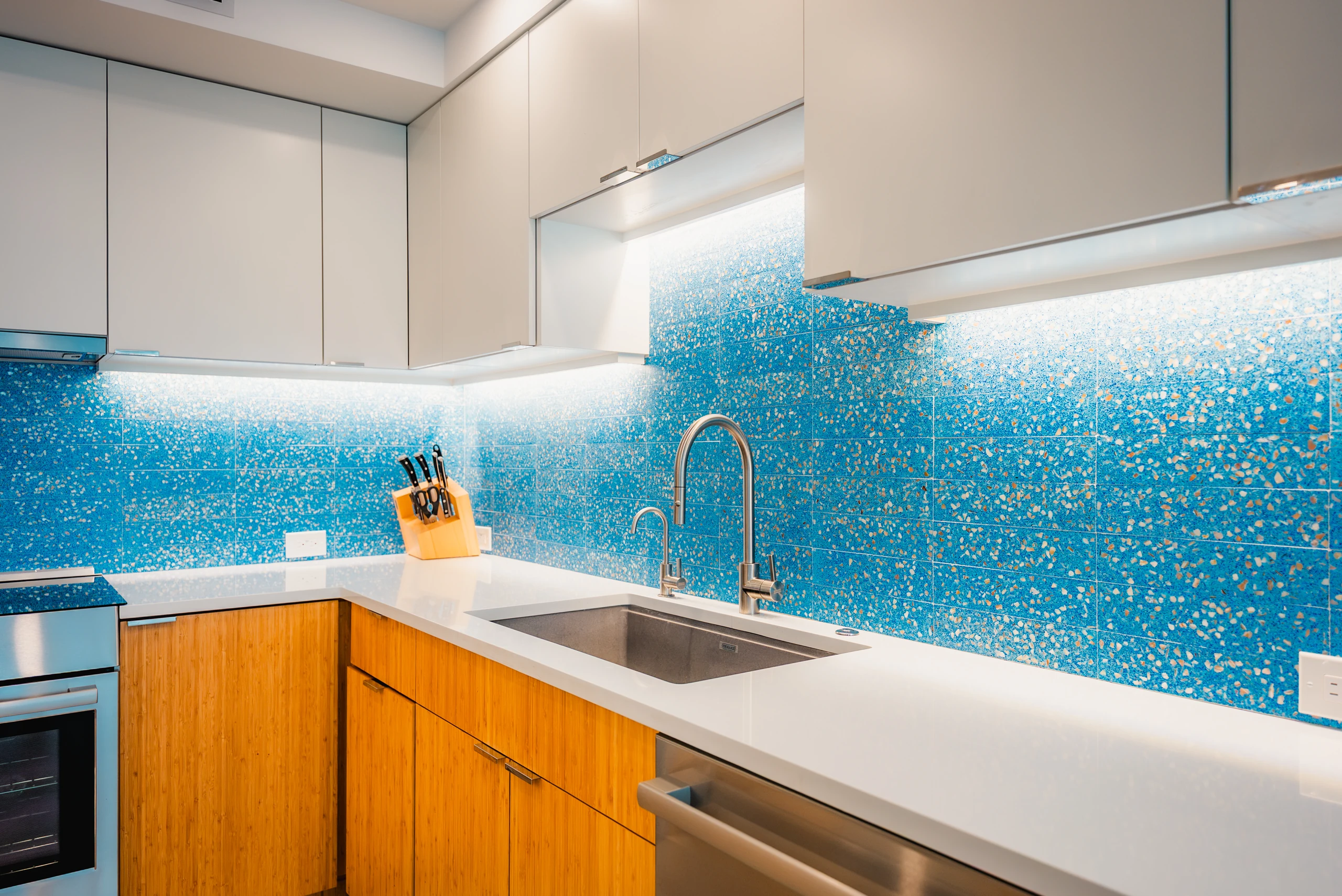 Kitchen with a blue glass mosaic backsplash, wood cabinets and undercabinet lighting