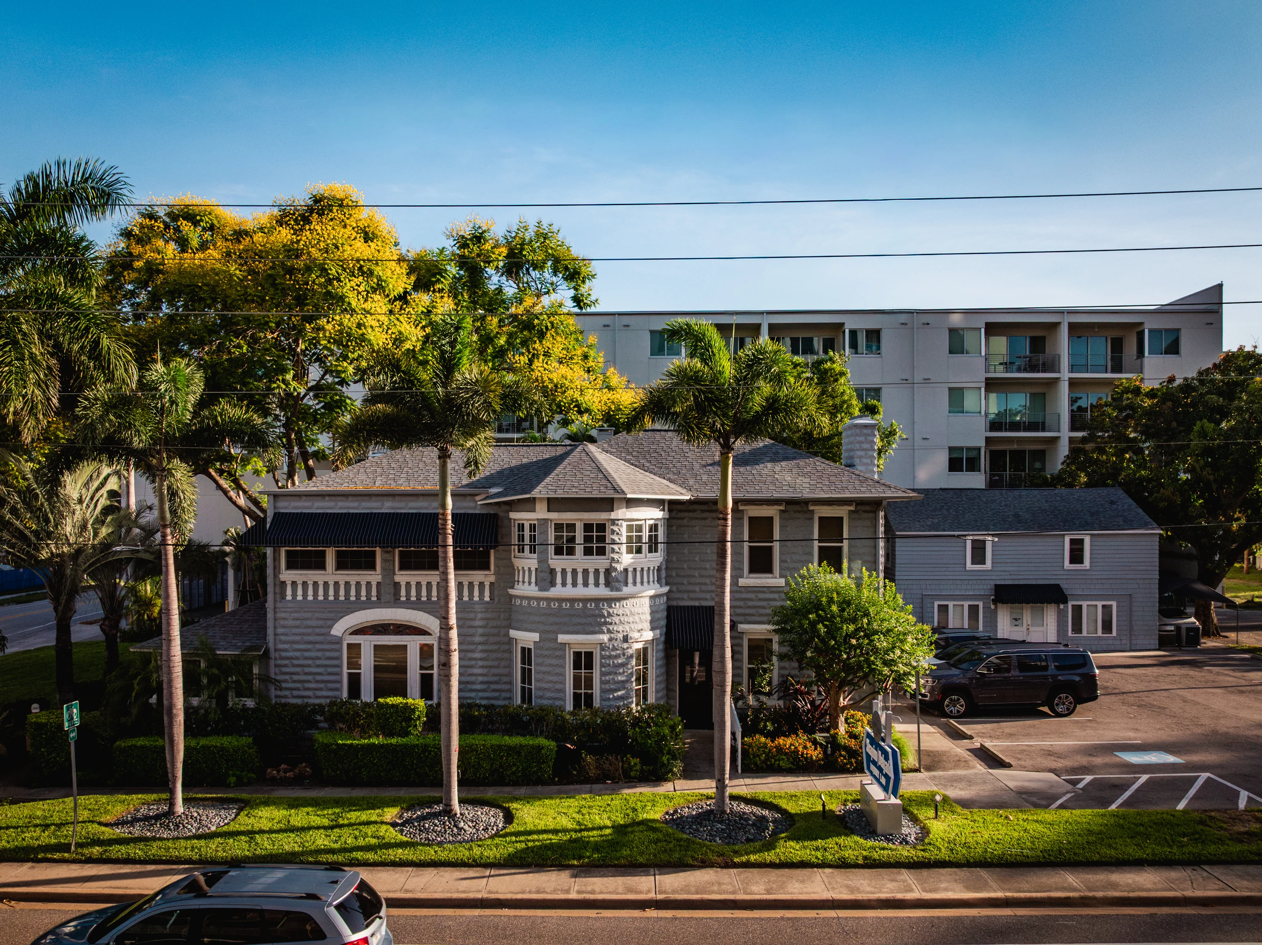 Two-story coastal home with a turret bay beside a palm-lined street