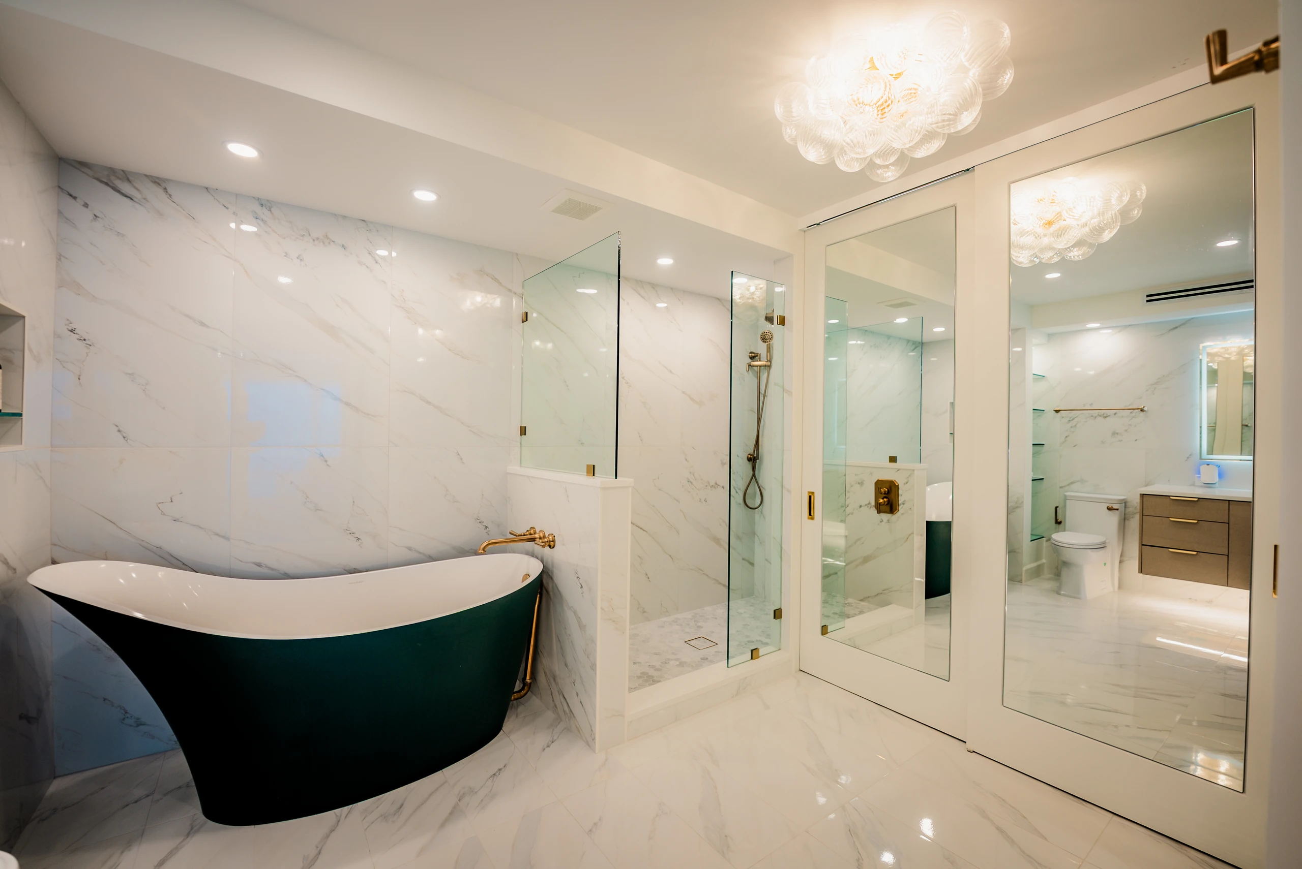 Bathroom with a green freestanding soaking tub and marble-tiled glass shower