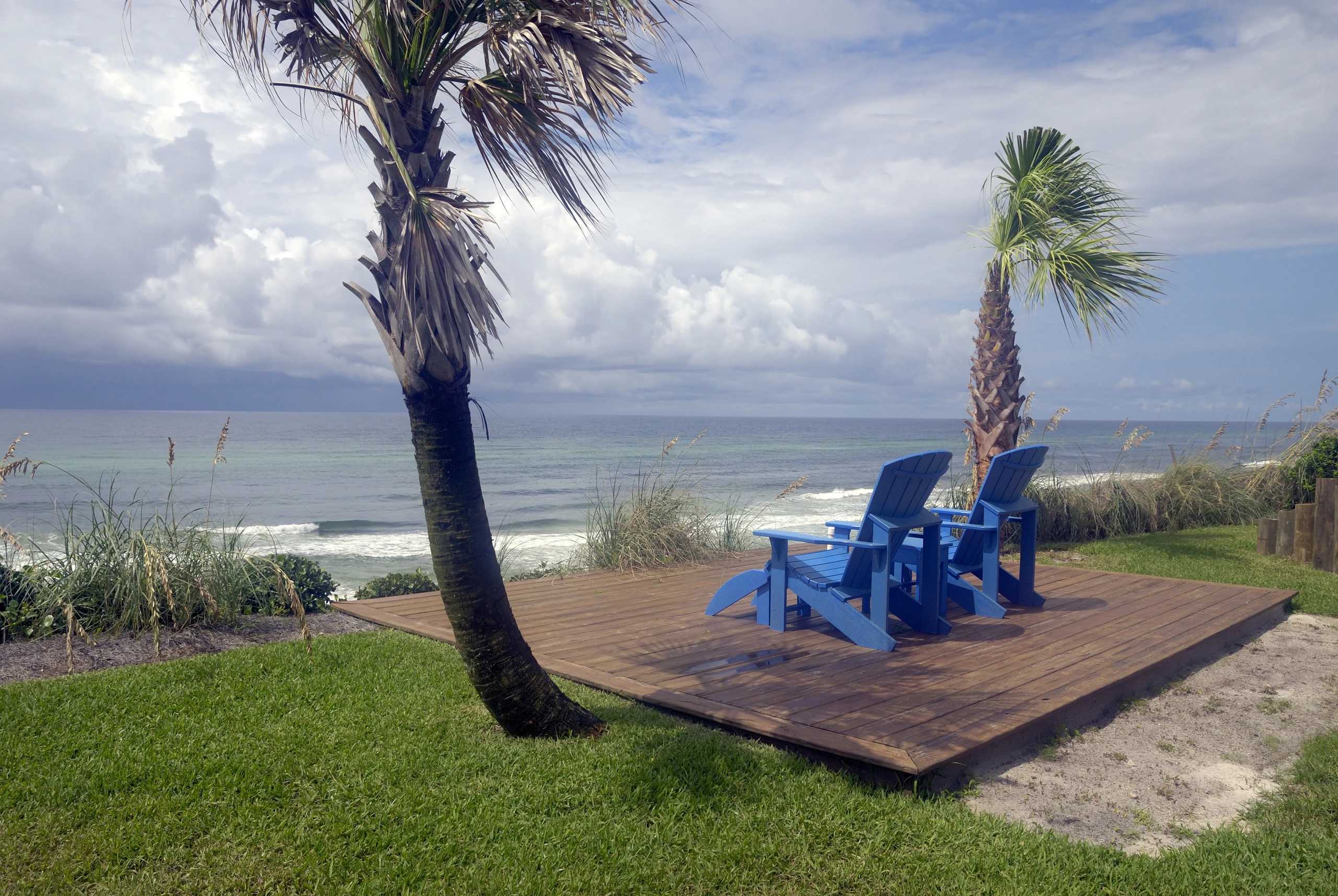 Wood deck with blue Adirondack chairs overlooking the Gulf beach
