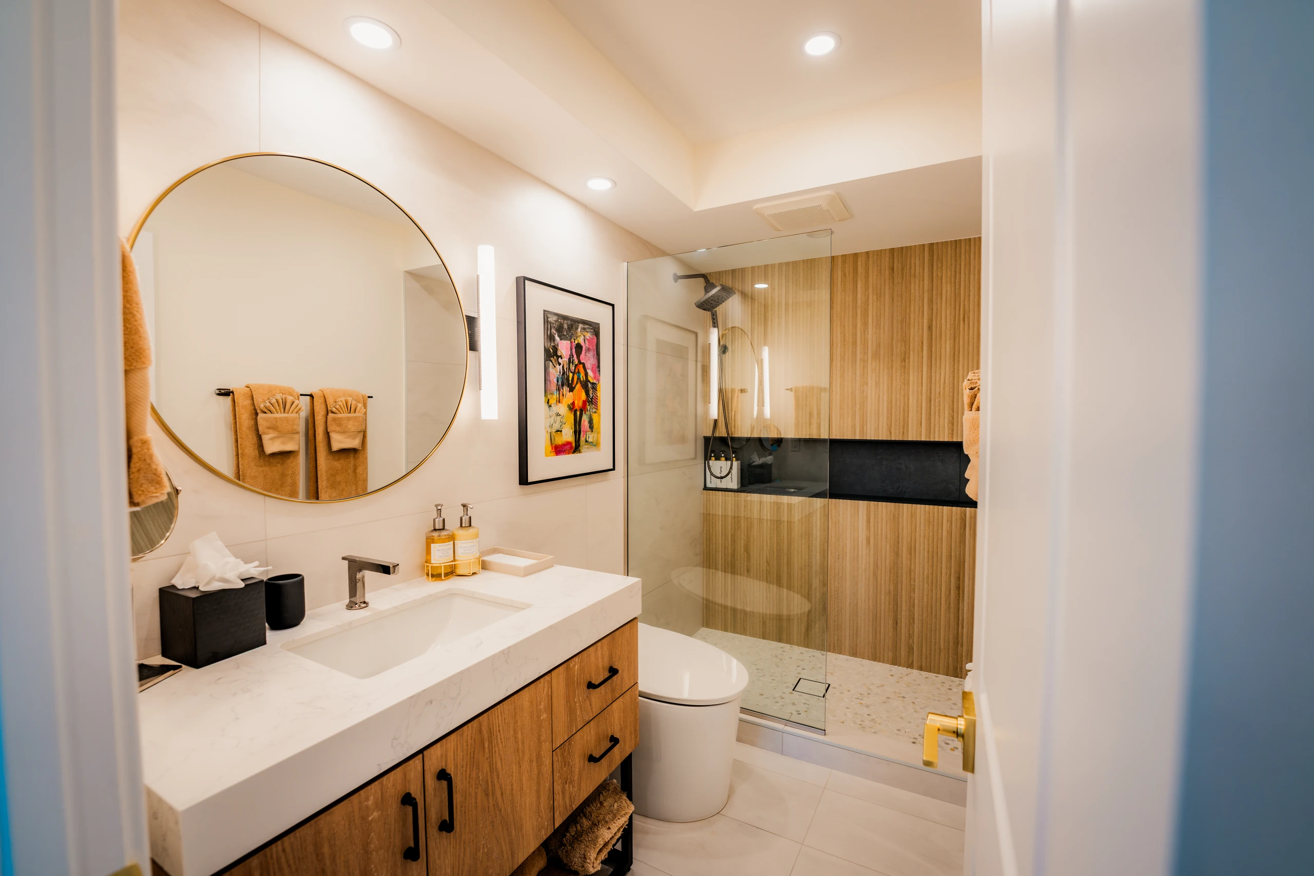 Remodeled bathroom with a round mirror, wood vanity and glass walk-in shower