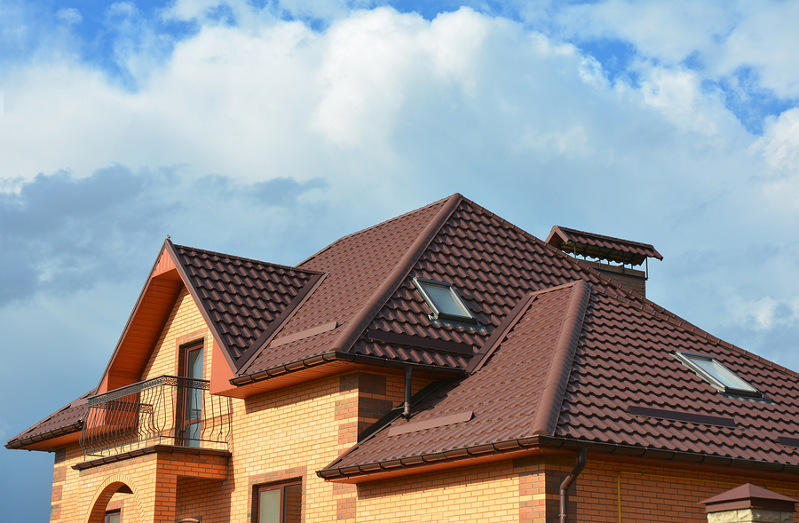 Brick home with a brown tile roof, dormers and skylights against a cloudy sky