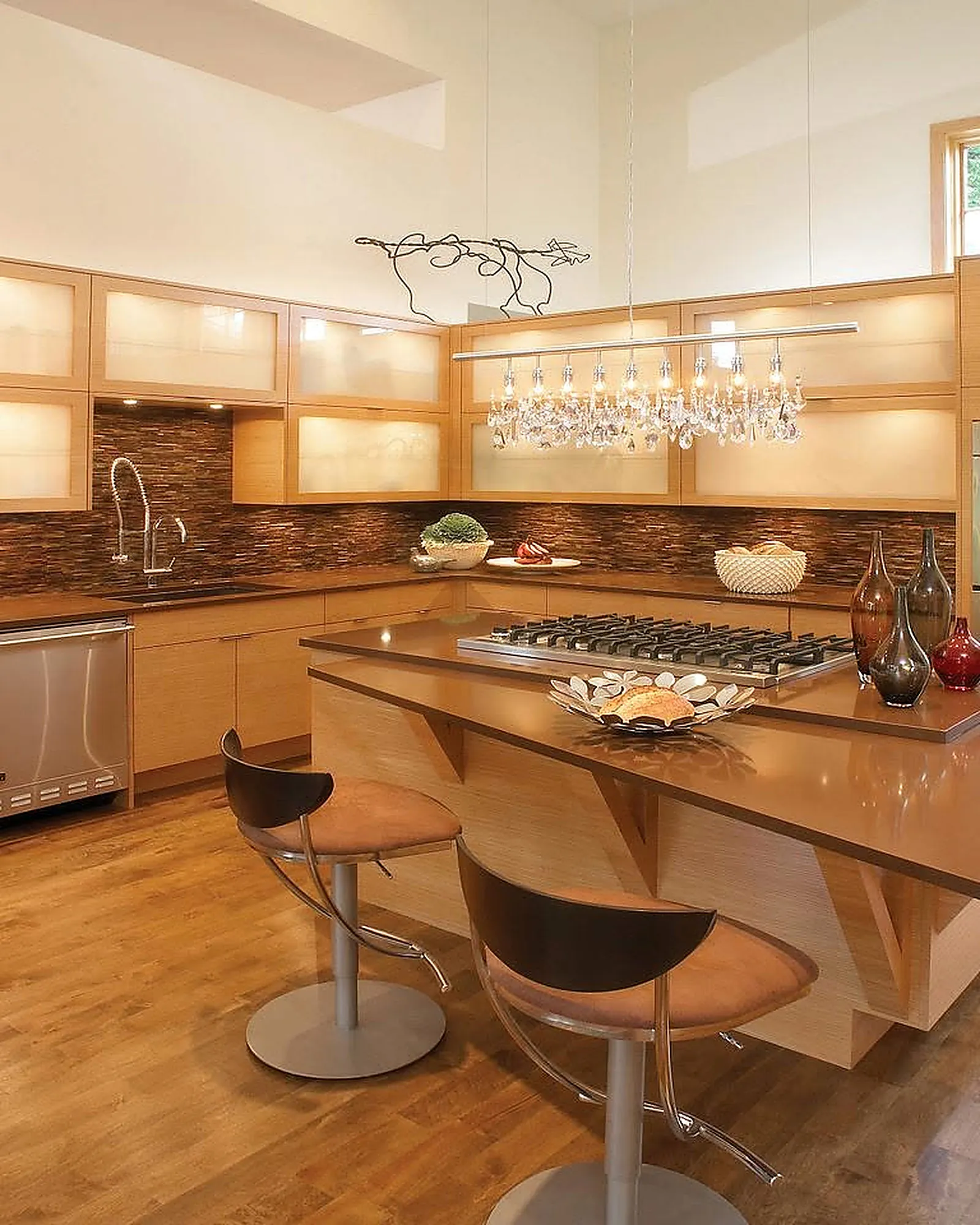 Contemporary kitchen with light wood cabinets, a crystal chandelier and bar seating