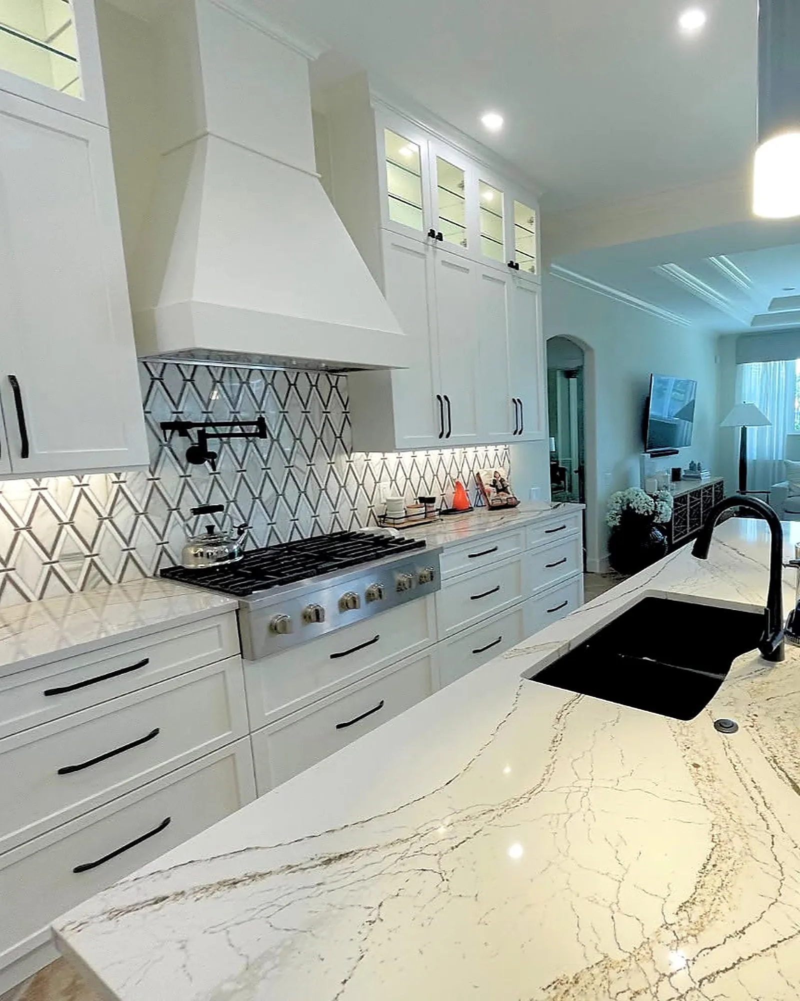 White kitchen with a plaster range hood, geometric backsplash and quartz counters