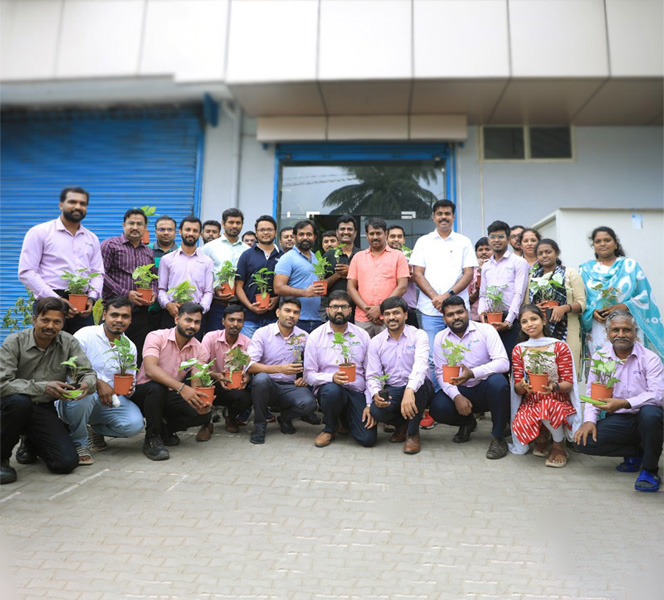 Group of people posing outdoors holding small potted plants in front of building with blue shutters.