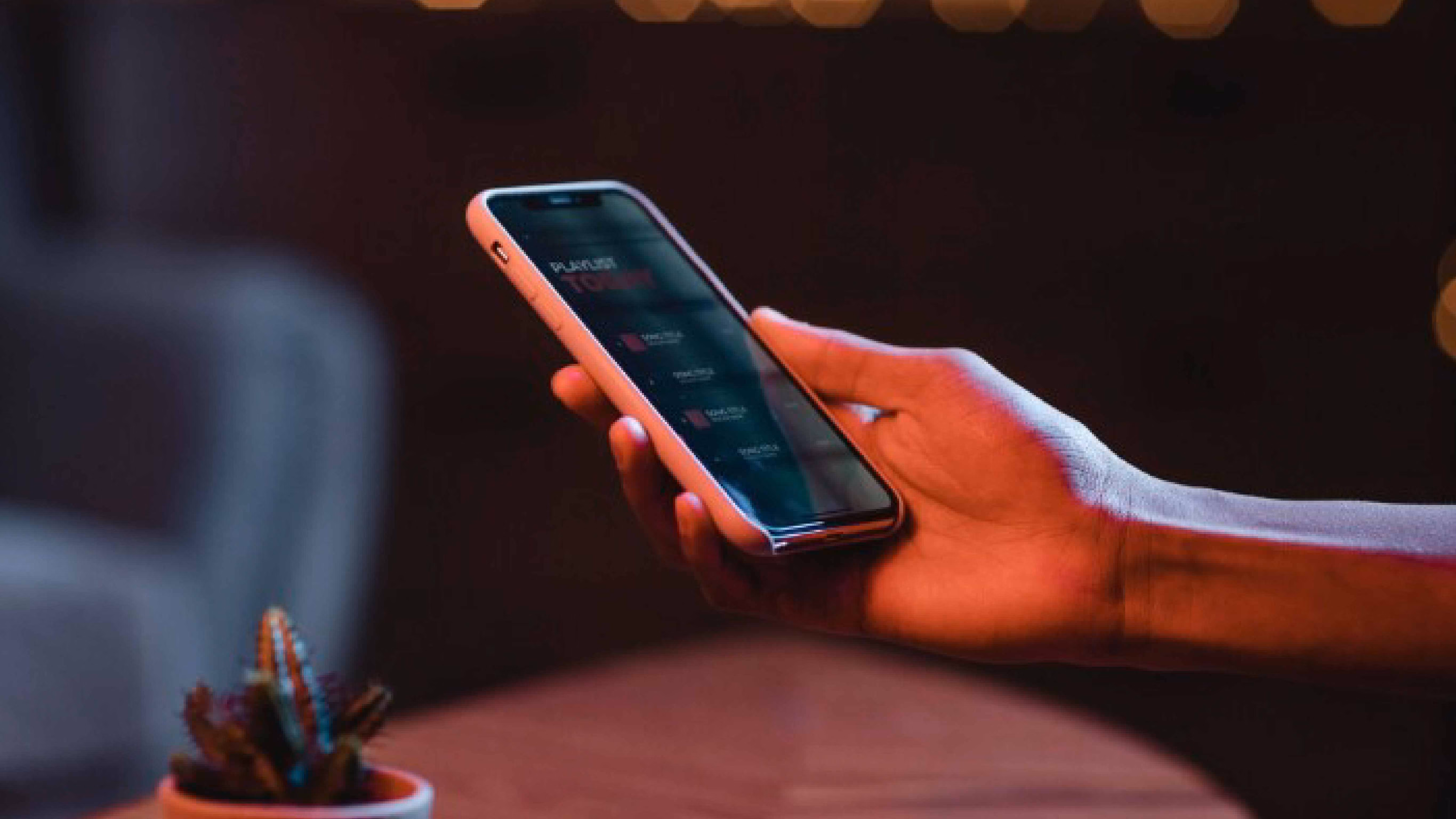 Hand holding smartphone displaying a dark mode app interface in a dimly lit setting.