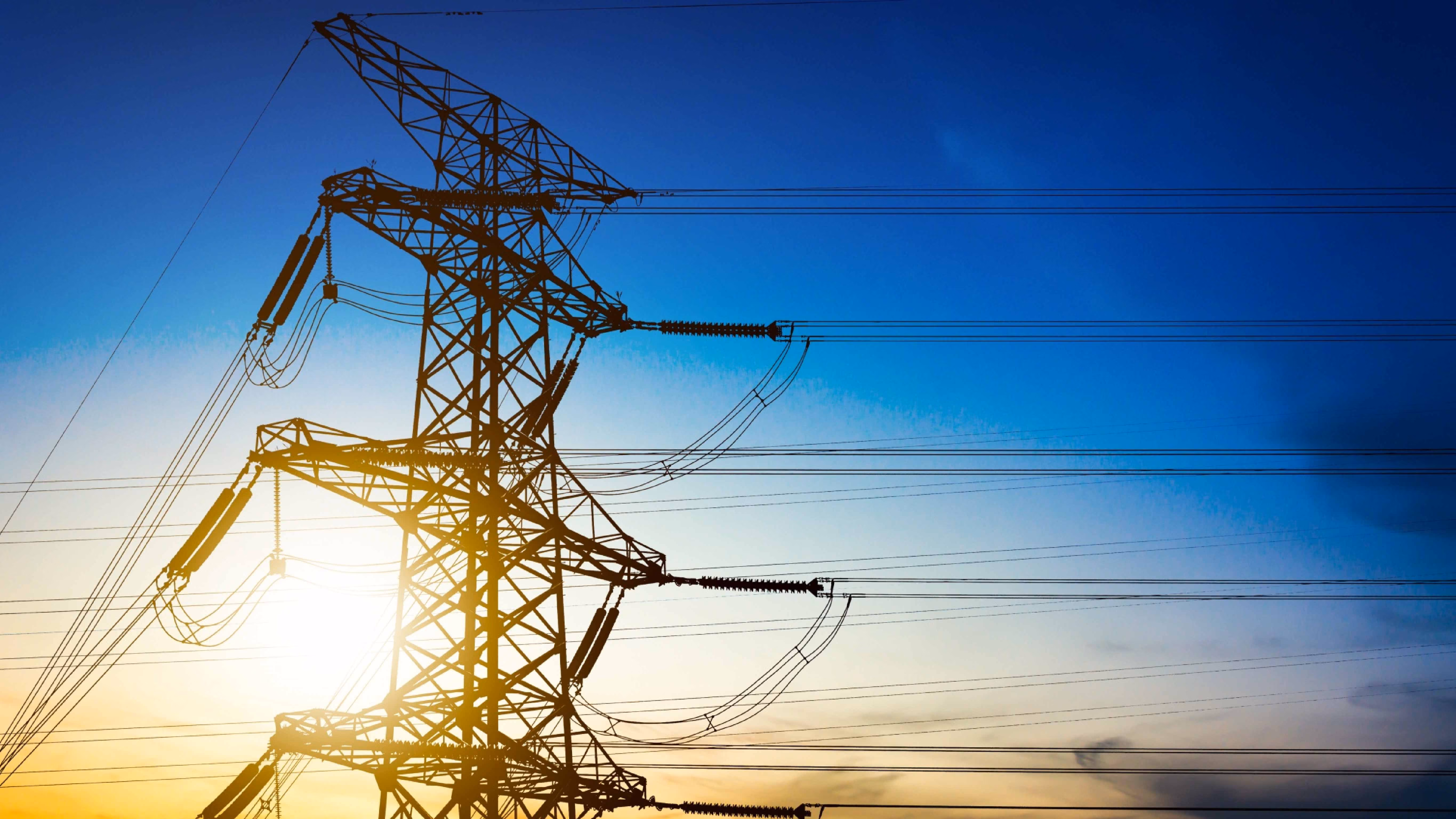 A high voltage electrical transmission tower with power lines against a sunset sky.