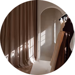 Sunlight casting shadows through curtains onto a minimalist archway and hanging clothes.