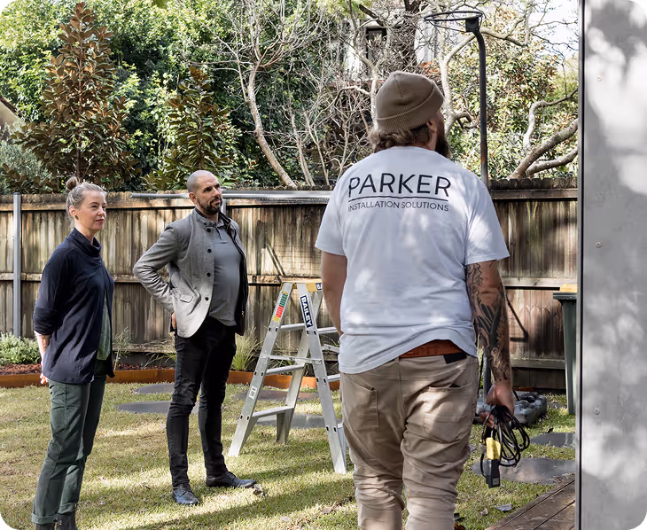 Three people in a backyard with a ladder; one wears a shirt reading Parker Installation Solutions.