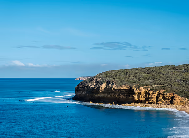 Rocky headland with greenery extending into blue ocean under a clear sky.