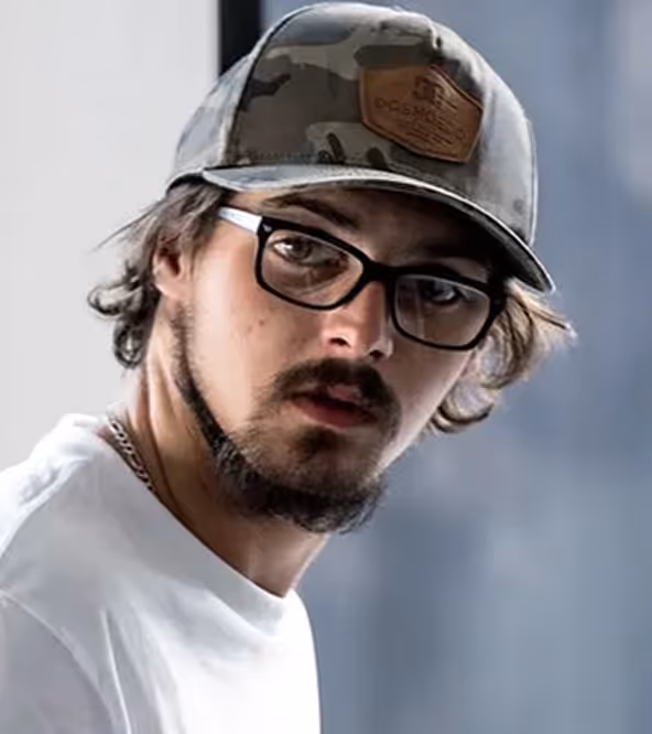 Young man with black glasses and a camouflage cap looking toward the camera in a white shirt.
