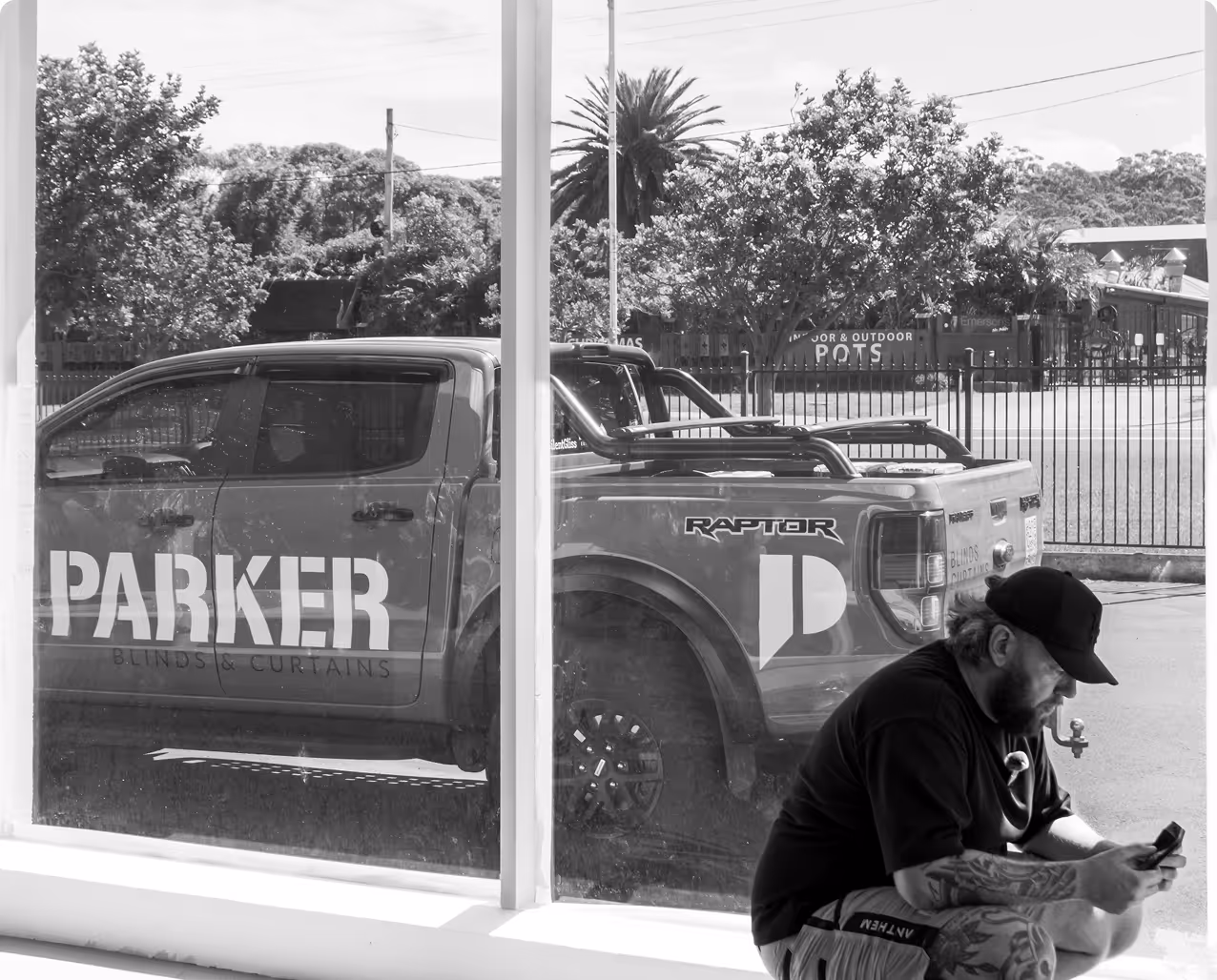 Man with tattoos sitting indoors near a large window looking at his phone, with a Parker truck outside.