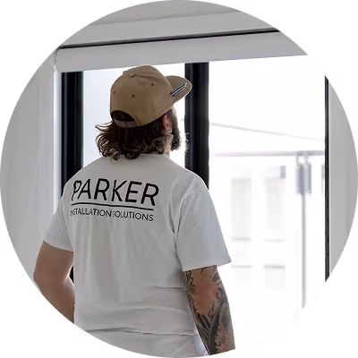 Man wearing a Parker Installation Solutions shirt adjusting window blinds indoors.