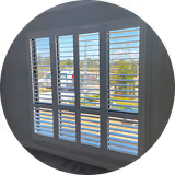 White plantation shutters covering three windows with a view of buildings and trees outside.
