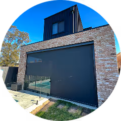 Modern house with stone facade and large dark glass garage door under bright blue sky.
