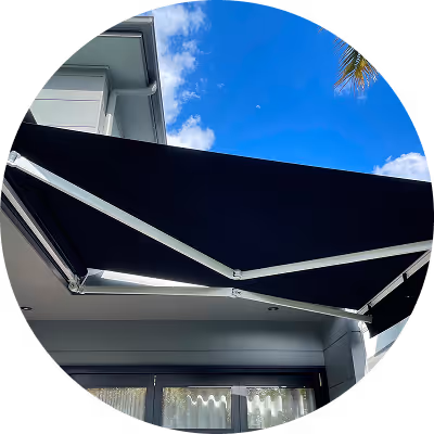Retractable black fabric awning extended over a patio door against a blue sky with clouds.