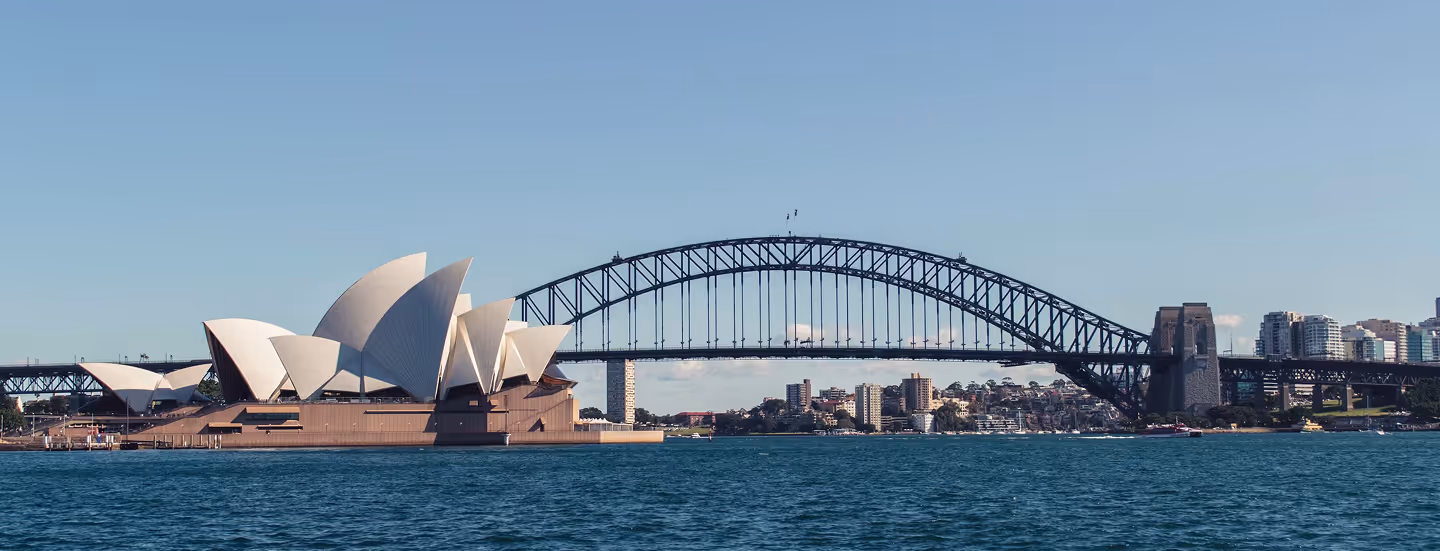 Sydney Opera House and Sydney Harbour Bridge over water under clear blue sky.