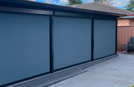 Outdoor retractable awnings in blue covering a patio area next to a house with a tiled roof.
