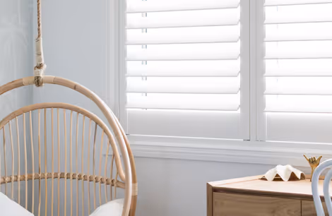 White window shutters with a bamboo hanging chair and wooden table beside it.